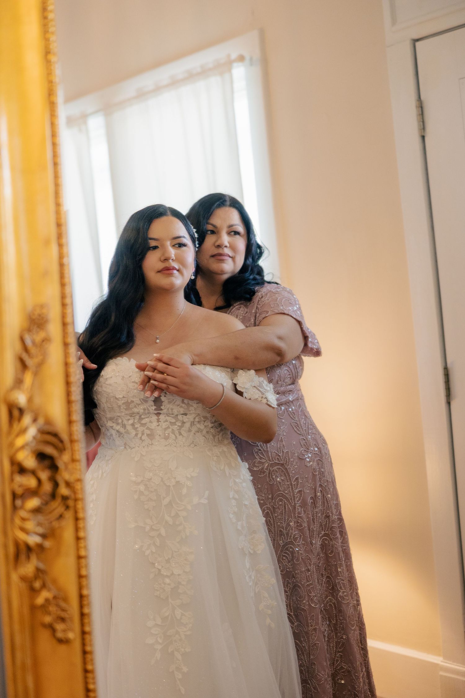 Beautiful lace wedding dress with delicate details being adjusted in front of a gold mirror.