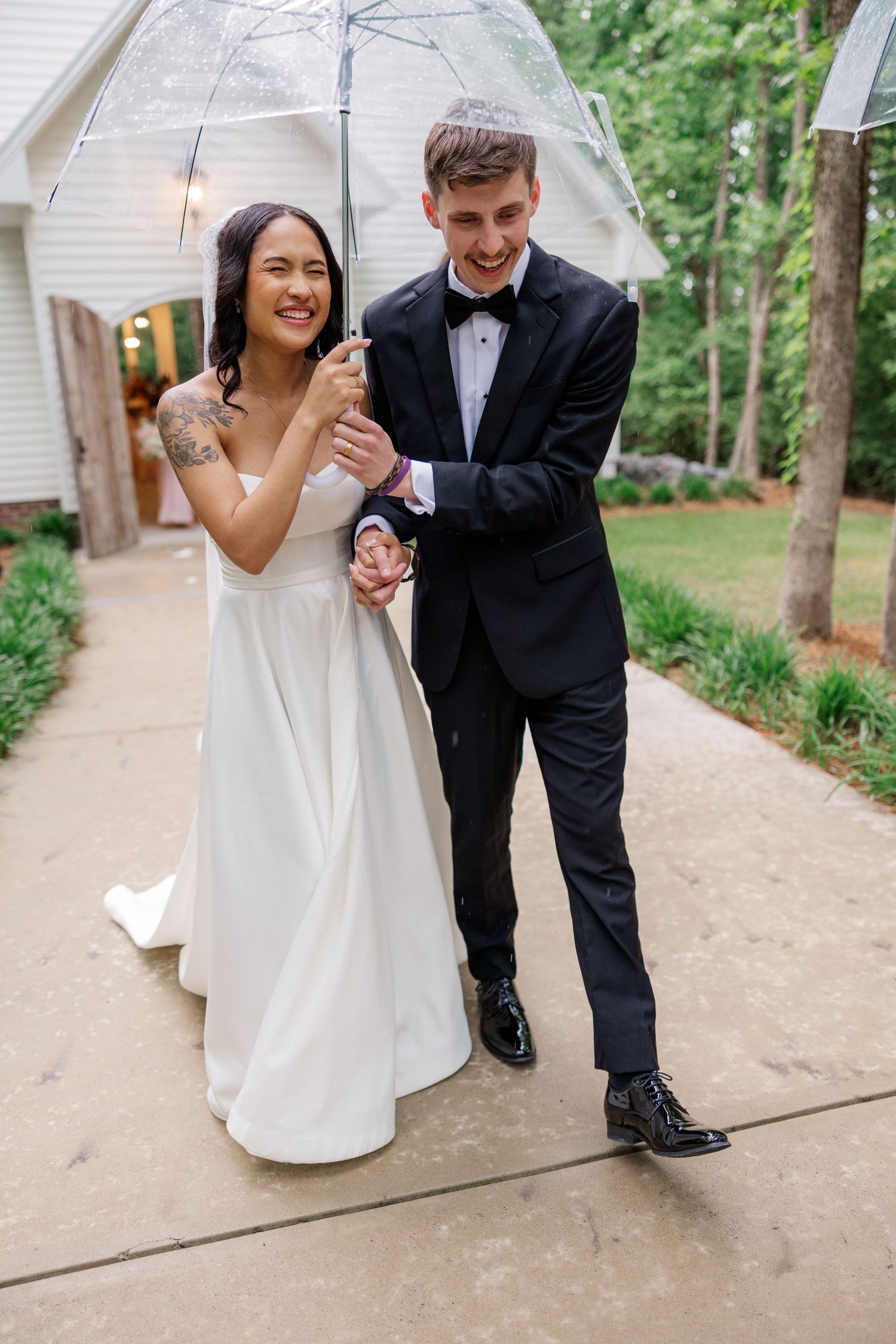 Wedding couple shares playful moments walking along outdoor pathway surrounded by trees.
