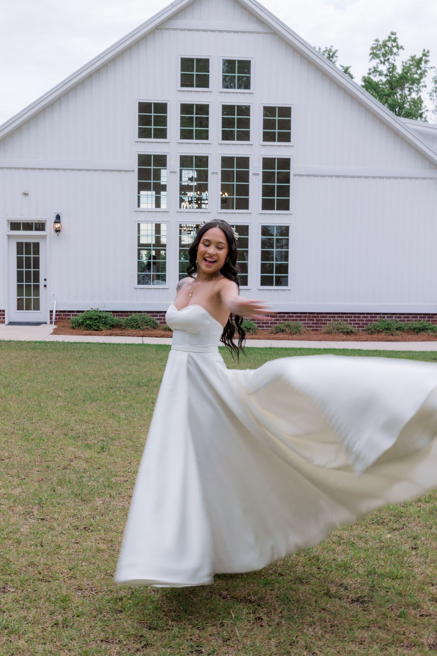 A flowing white wedding dress twirls gracefully against a white chapel building and green lawn backdrop.