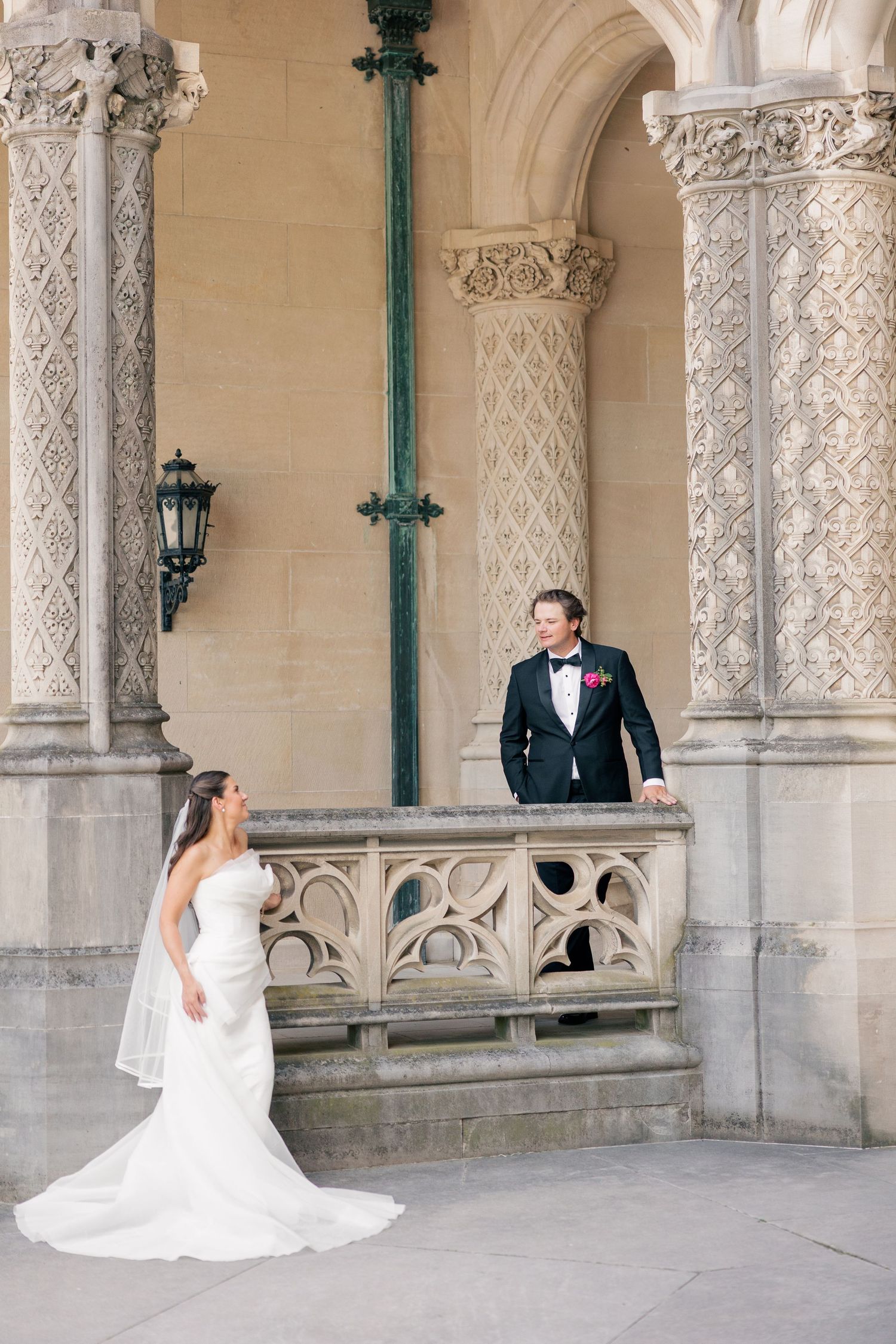 Bride and groom share romantic moment among ornate stone columns at elegant wedding venue.