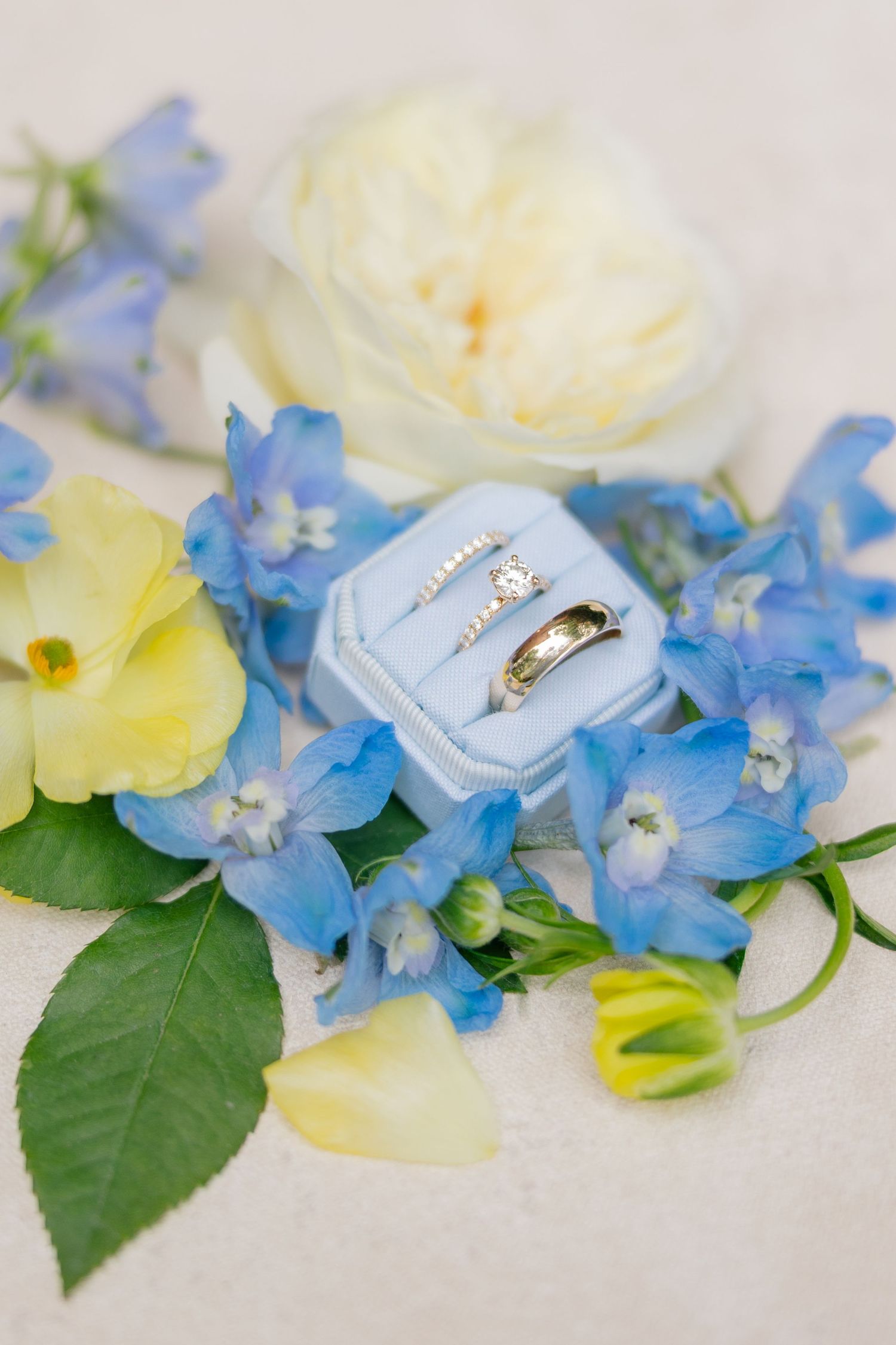 Wedding rings in blue velvet box surrounded by blue and yellow flowers.
