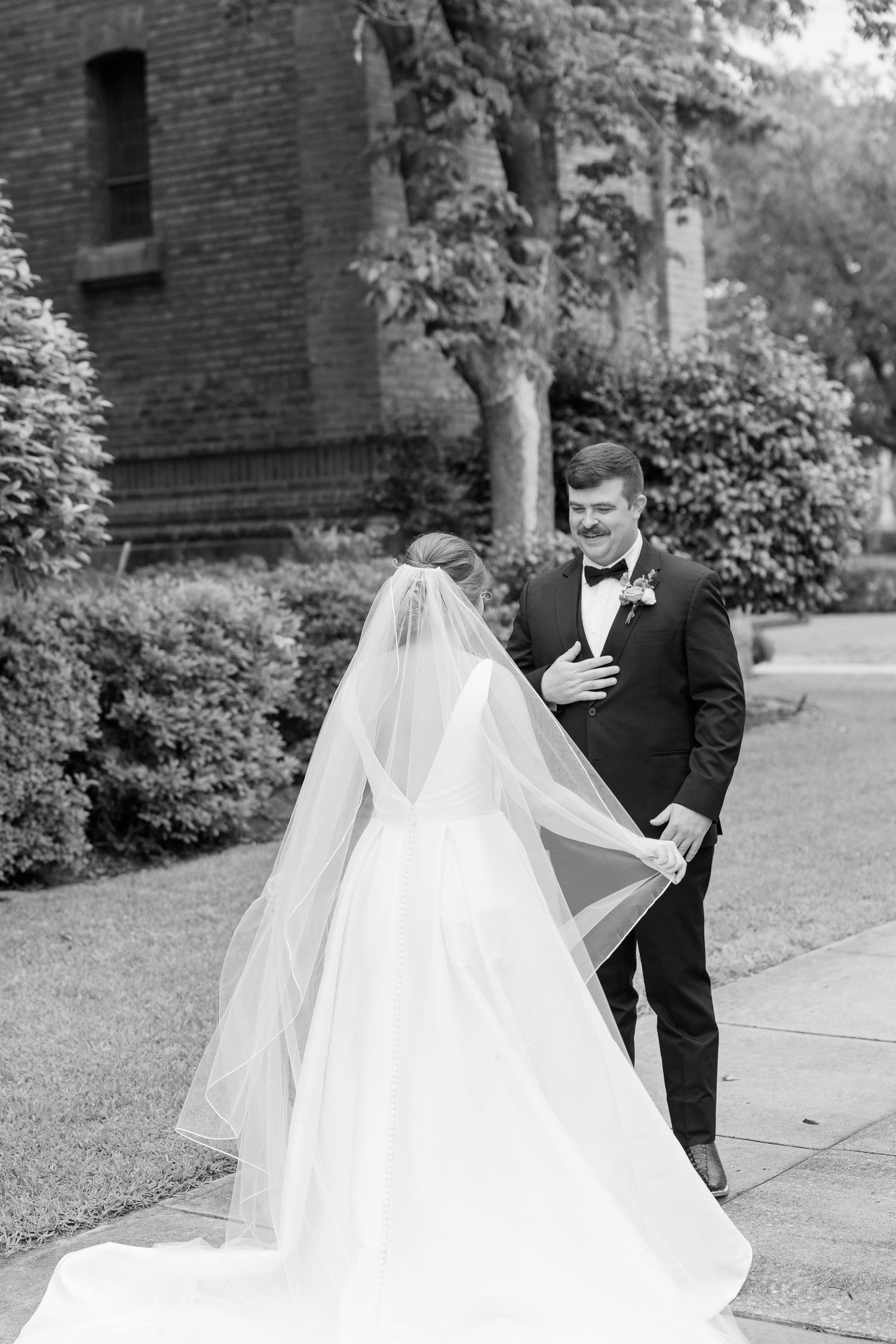 Black and white photo of a groom reacting emotionally during a first look with his bride in a flowing veil.