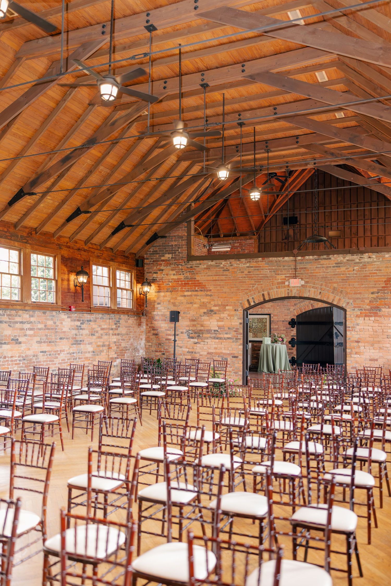 Elegant wedding ceremony setup with rows of chiavari chairs in a rustic brick venue with wooden vaulted ceiling.