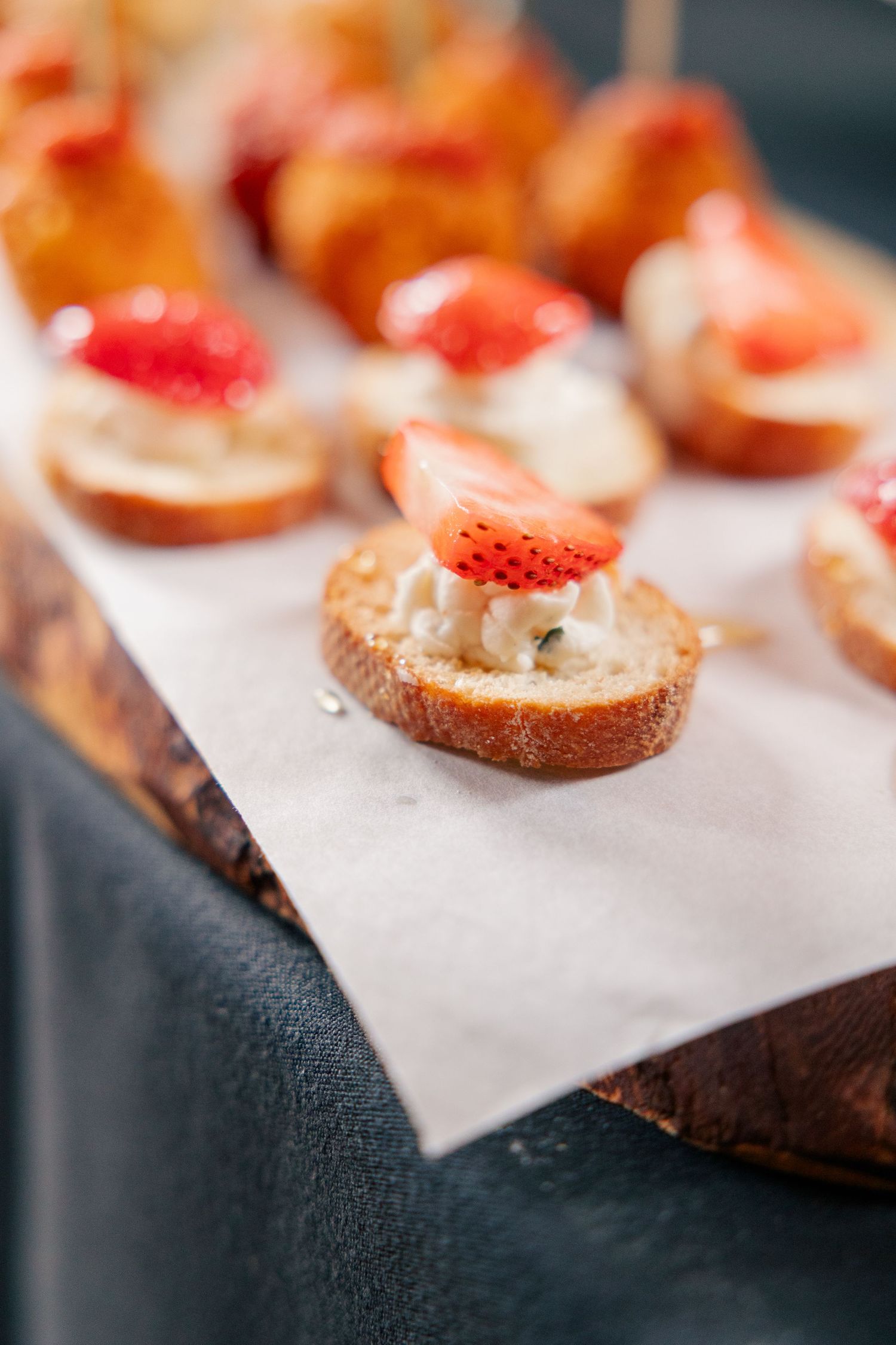 Elegant wedding appetizers of strawberry and cream cheese crostini displayed on rustic wooden serving board.