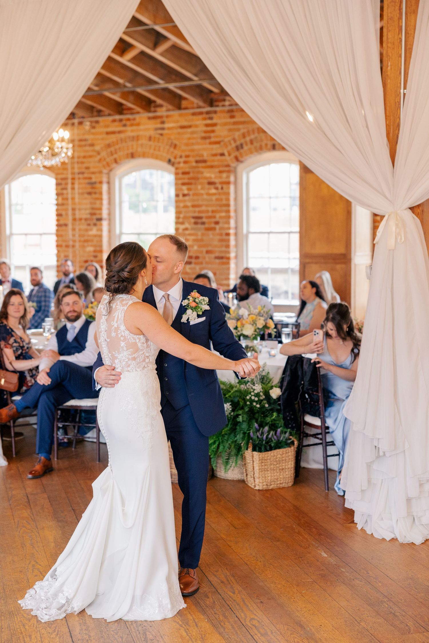 Bride and groom share first dance under white draping in elegant rustic brick wedding reception venue.
