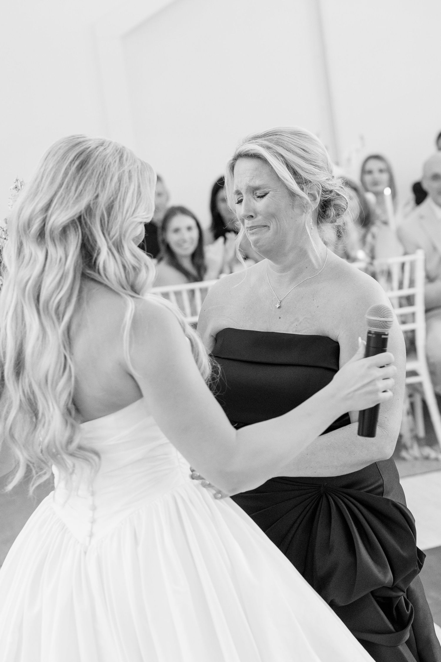 Emotional black and white photo of bride sharing tender moment with woman in black dress.