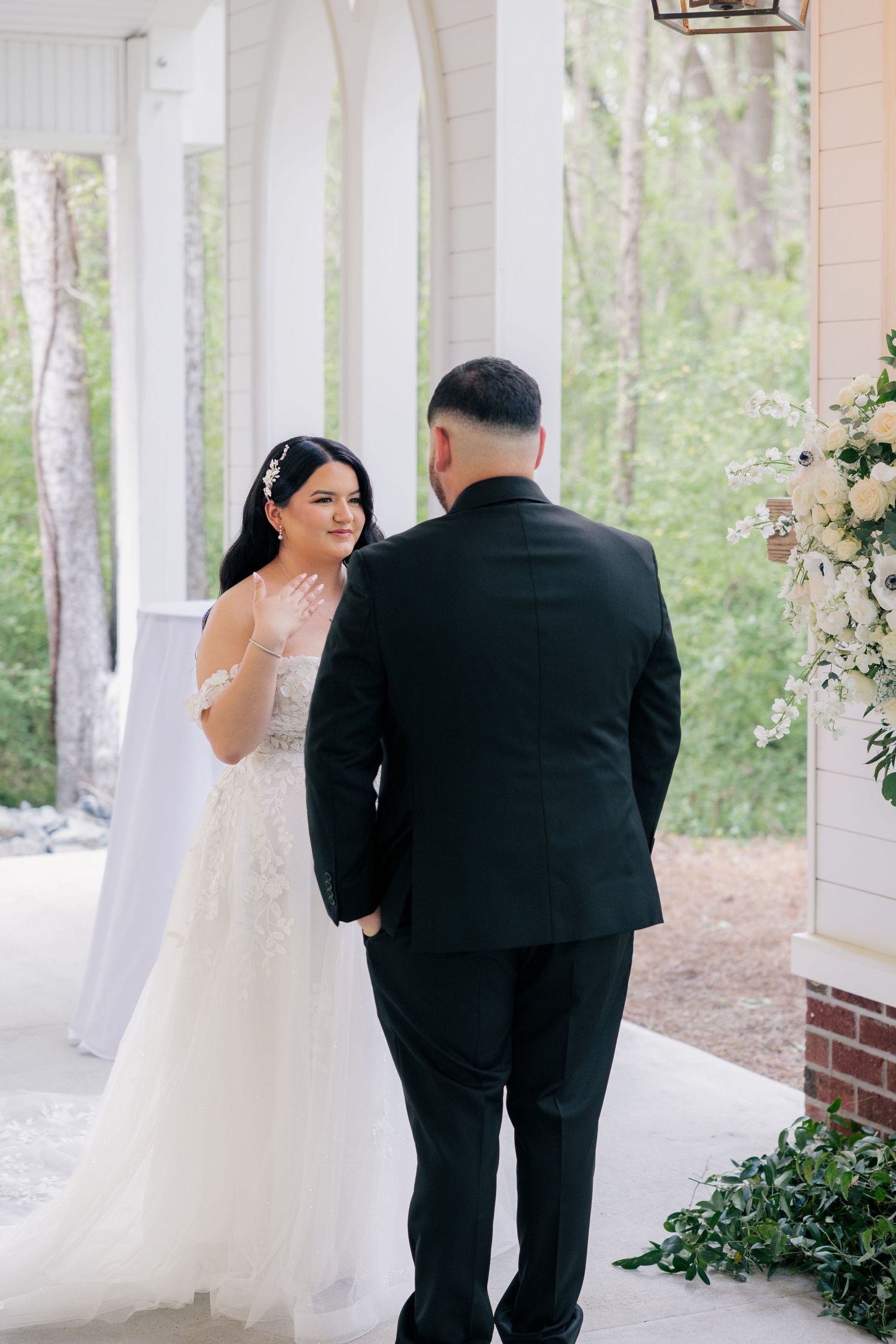 A couple shares a tender moment on a white columned porch surrounded by greenery.
