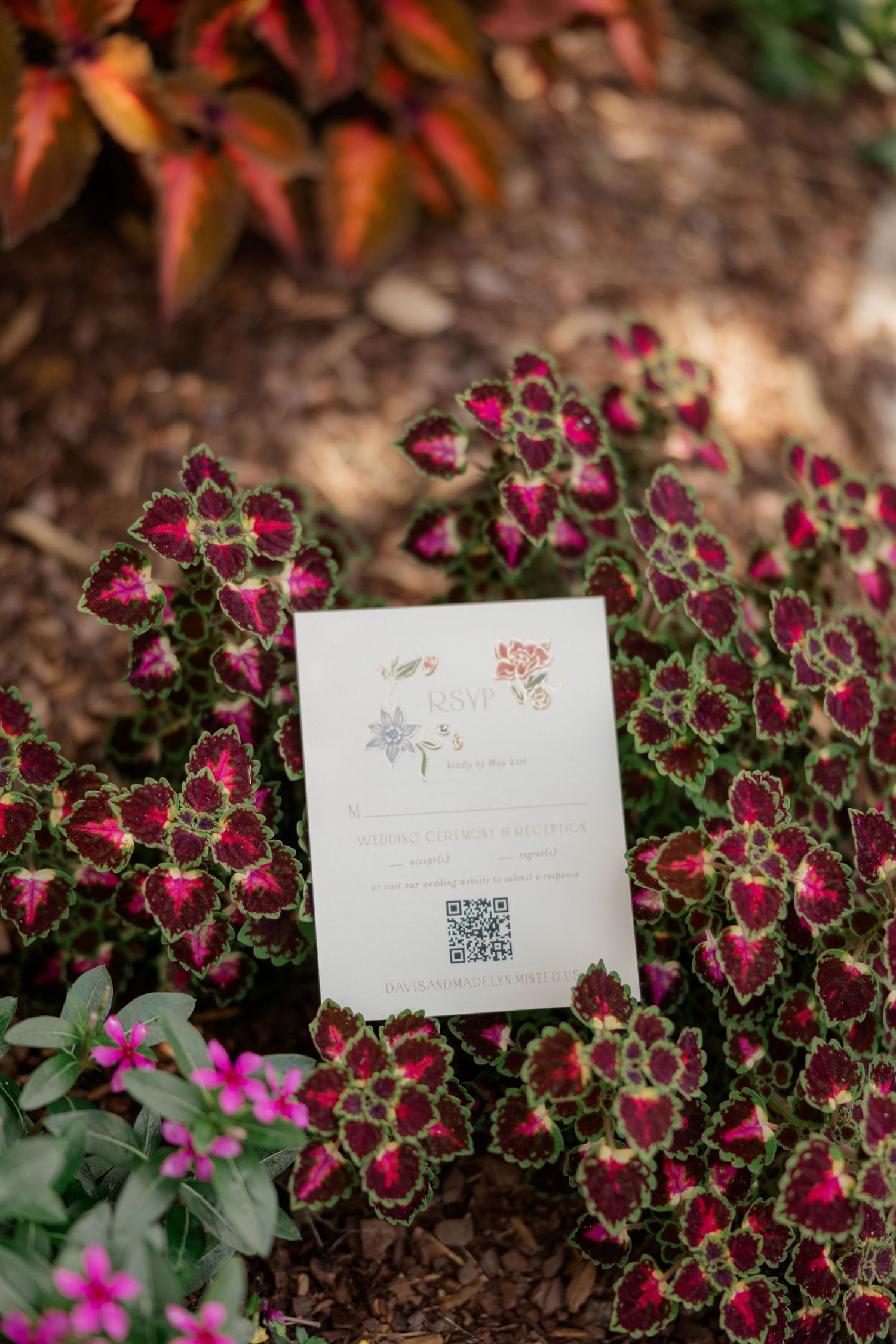 Wedding invitation cards displayed among burgundy flowers and greenery.