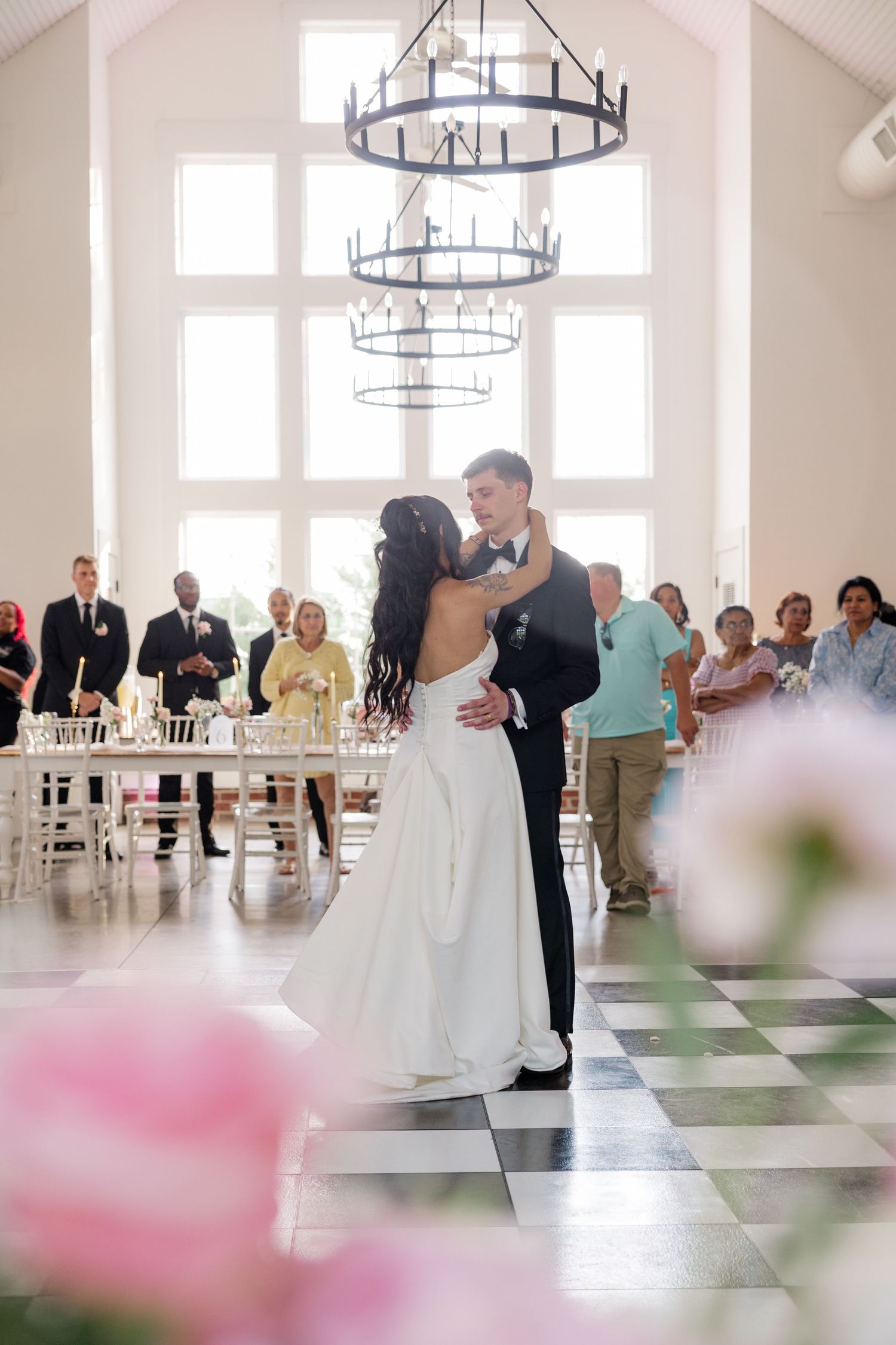 Wedding guests enjoying first dance in bright reception venue with chandeliers.