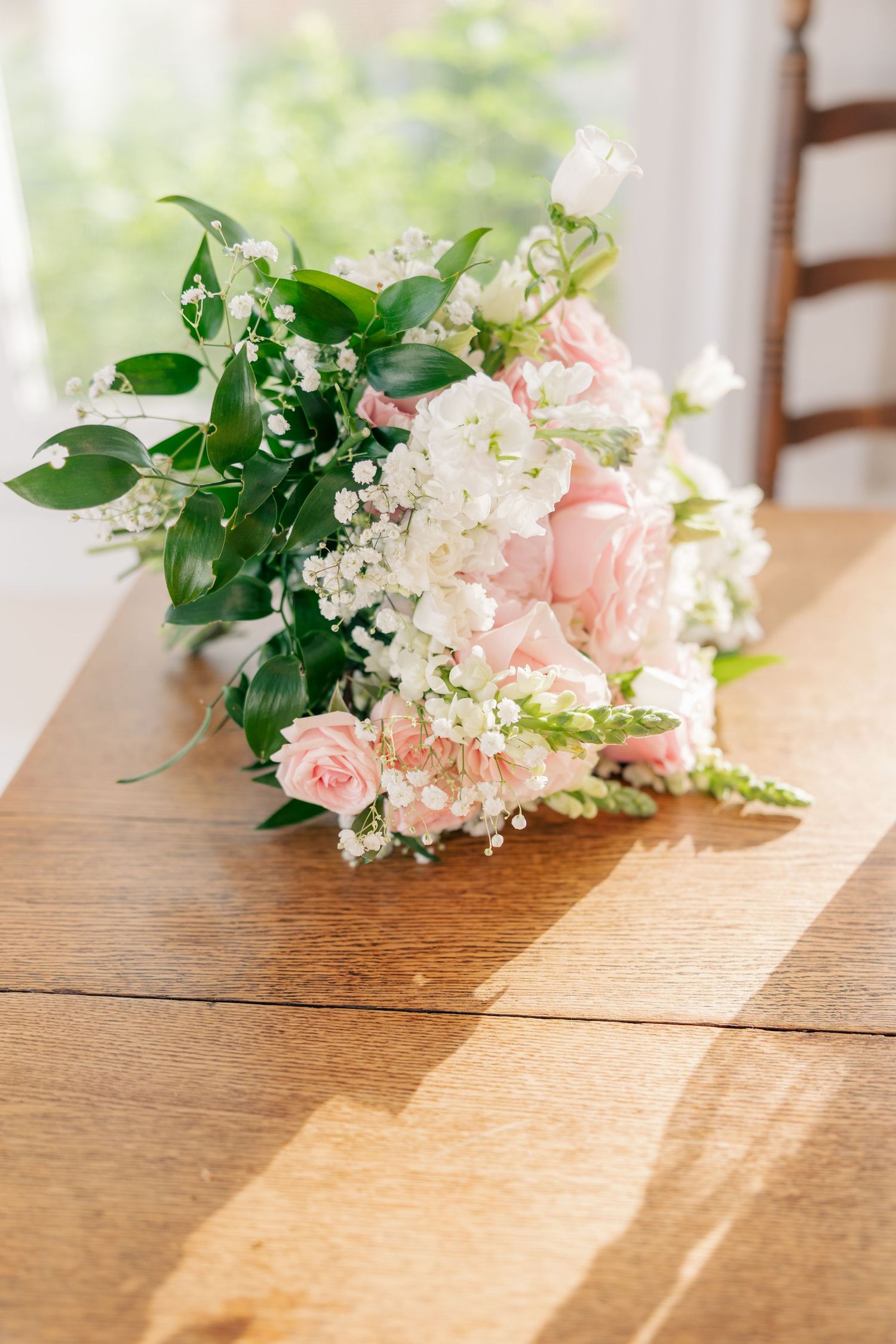 Fresh pink roses and white flowers arranged on a wooden table in natural sunlight.