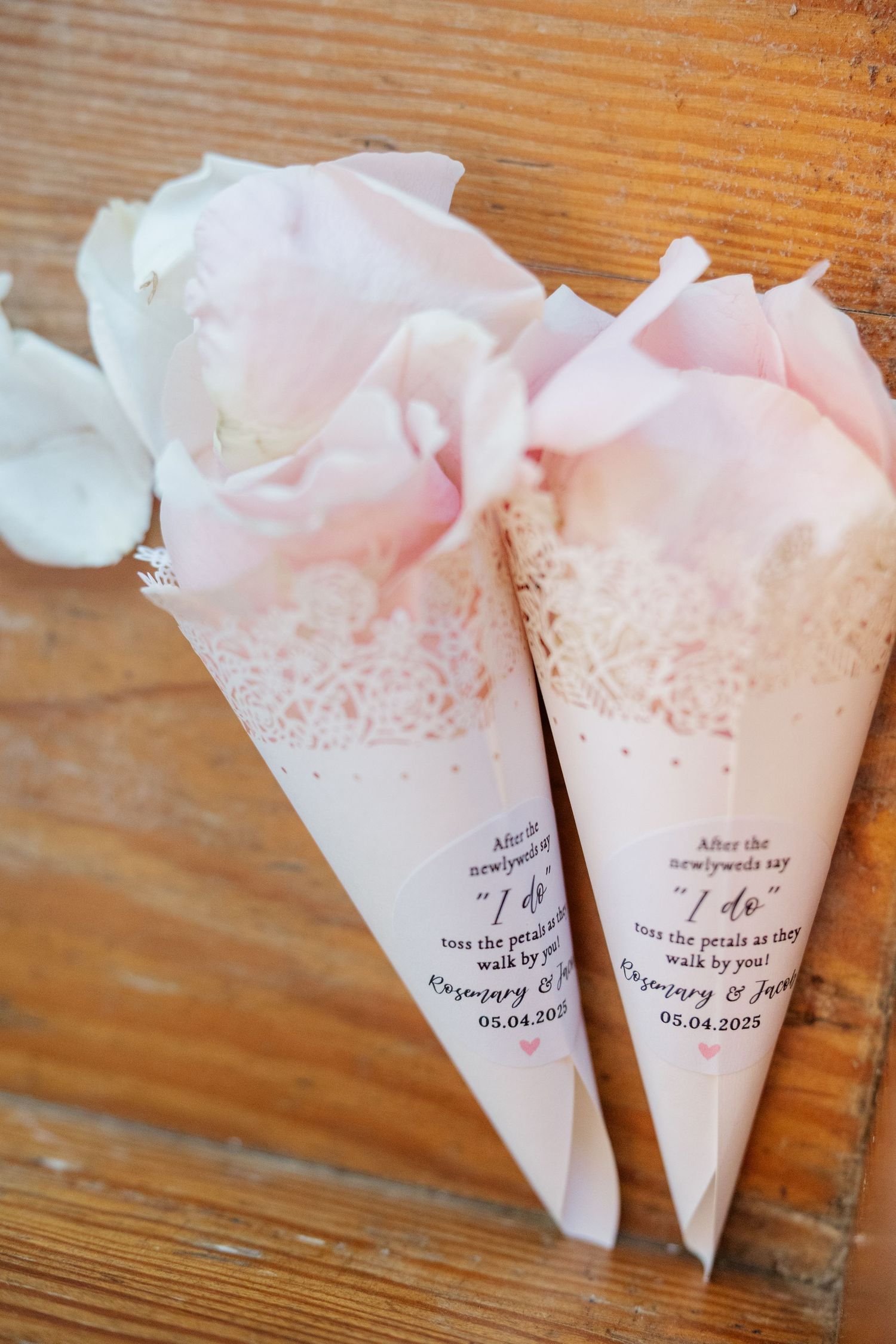 Delicate pink and white paper cones with lace trim and text details displayed on wooden surface.