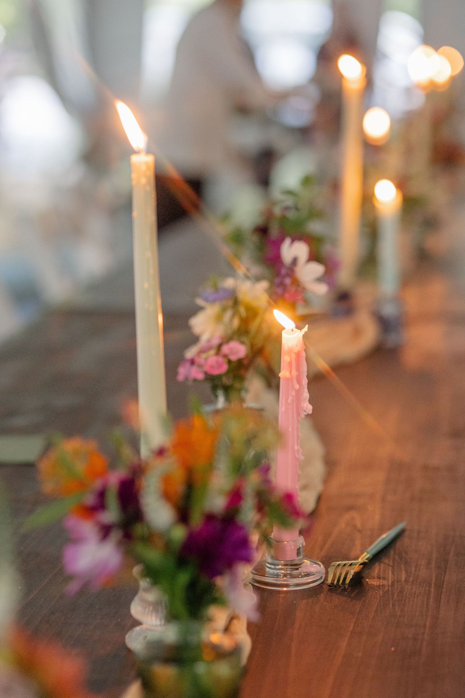Lit taper candles and colorful wildflower arrangements decorating a rustic wooden wedding reception table.