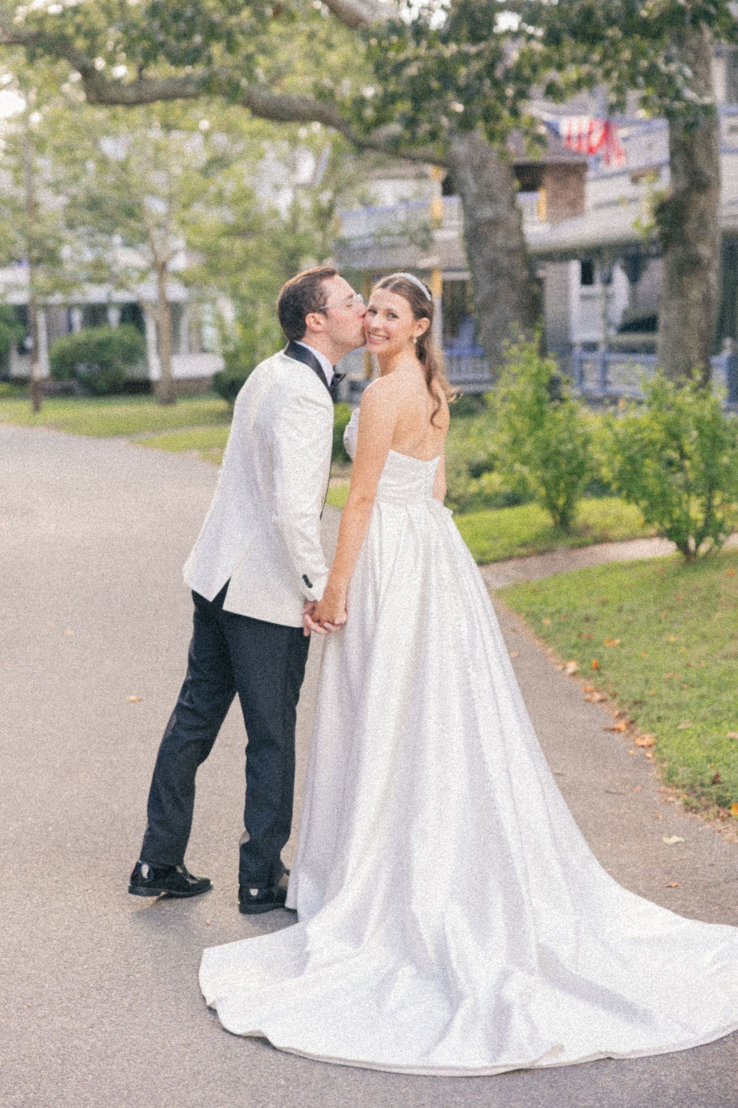 Groom in white jacket kisses bride on cheek as she smiles in a strapless gown with long train.