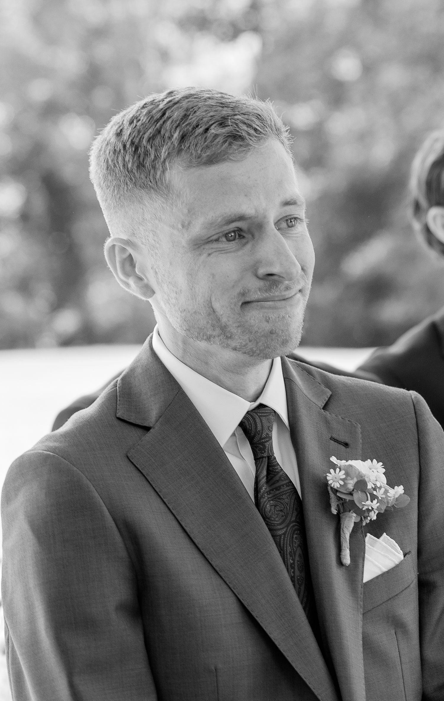 Black and white portrait of emotional groom watching bride walk down aisle at wedding.