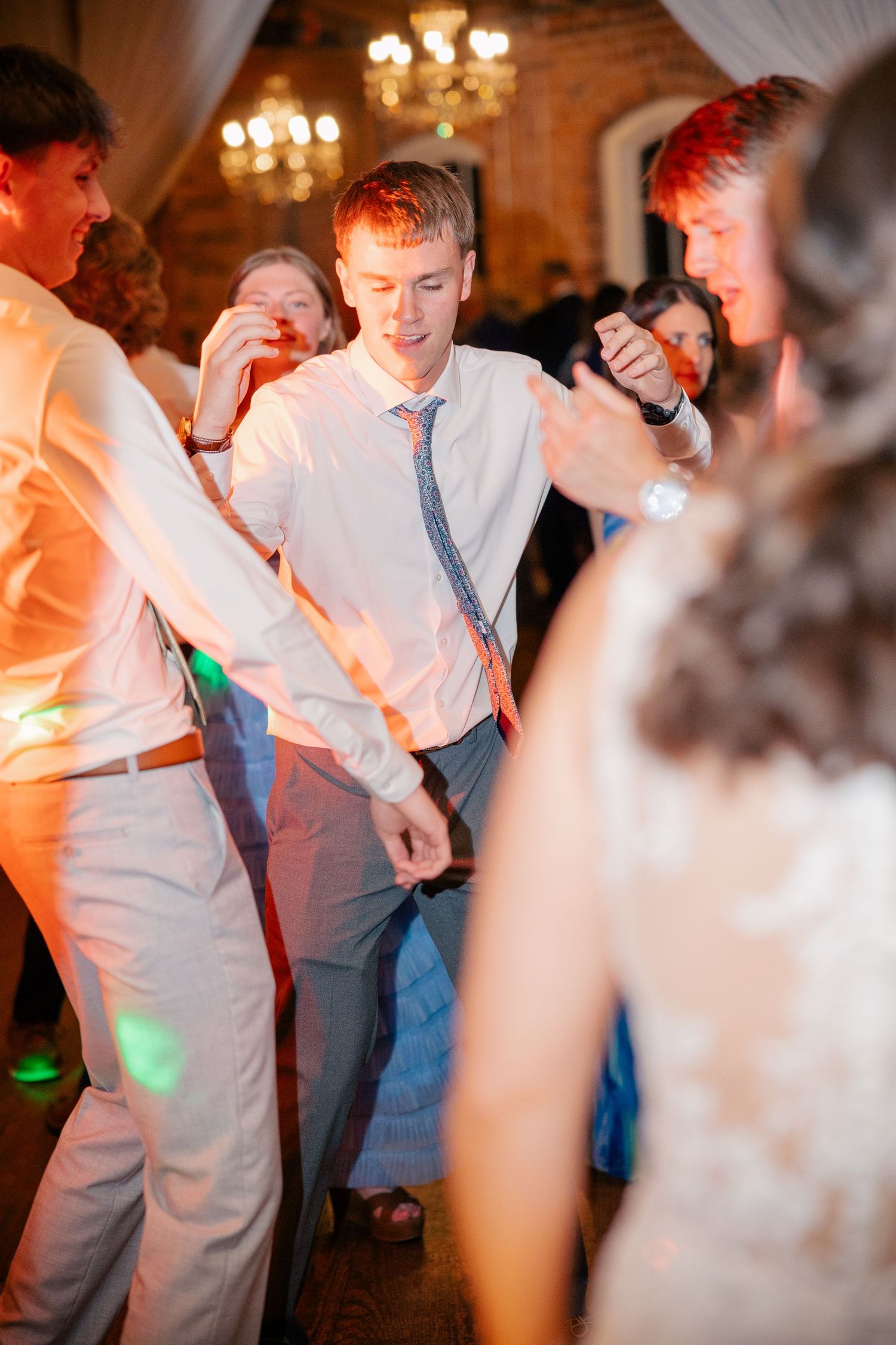 Wedding guests dance energetically under warm lights during lively reception celebration.