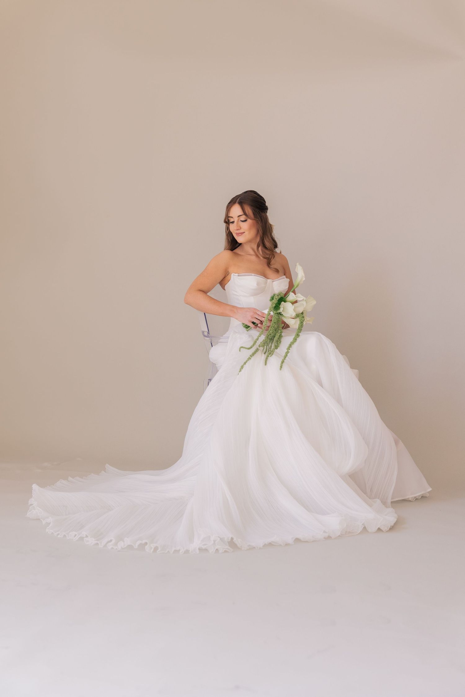 Beautiful bride in flowing white strapless ballgown poses with bouquet against neutral background in studio portrait.
