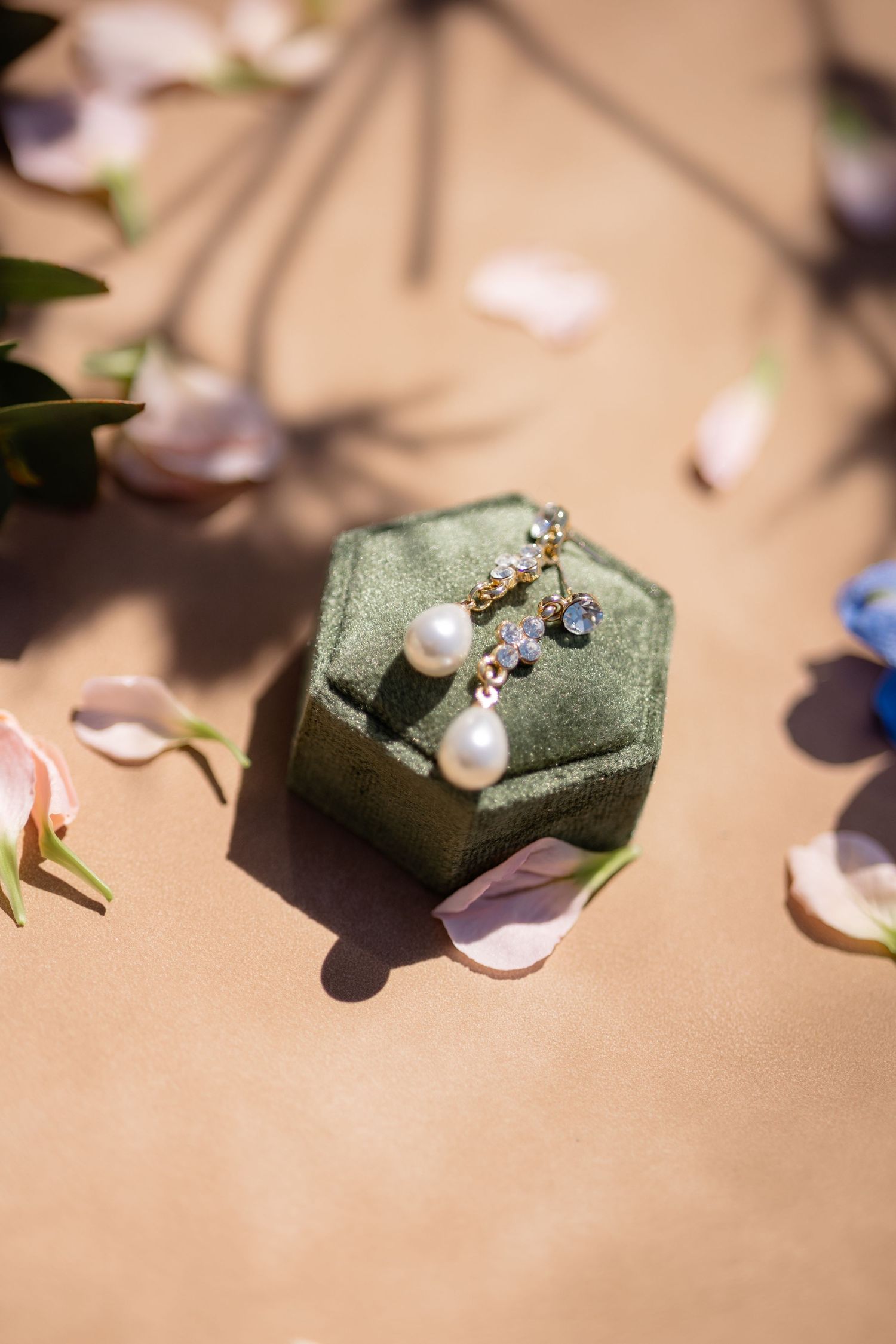 Delicate pearl and gemstone jewelry pieces displayed on sage green velvet cushions.