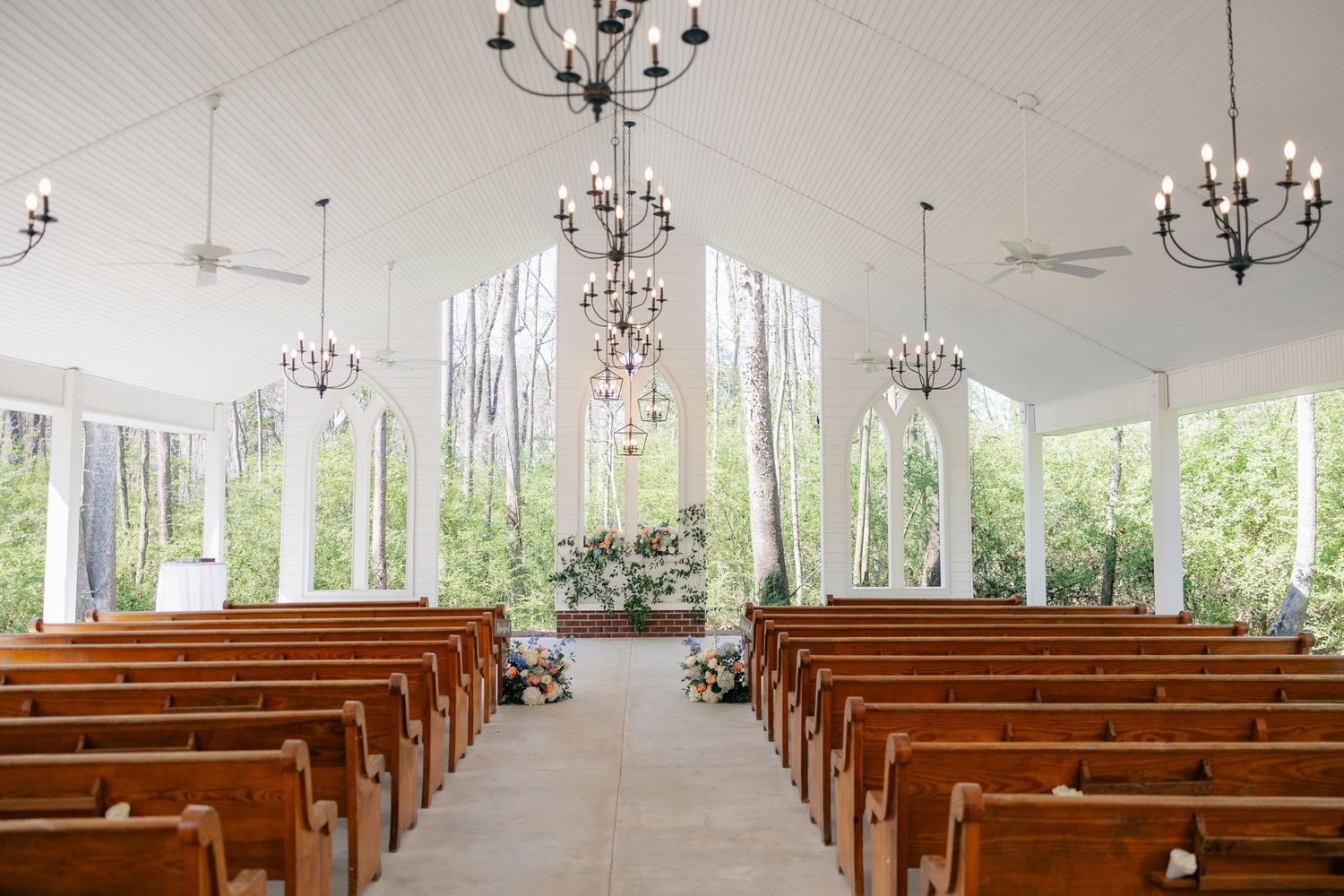 White chapel interior with rows of wooden pews and crystal chandeliers.