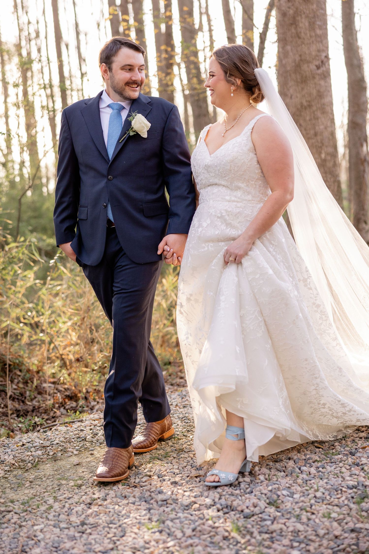 A couple laughs together on a gravel path during their wedding photoshoot.