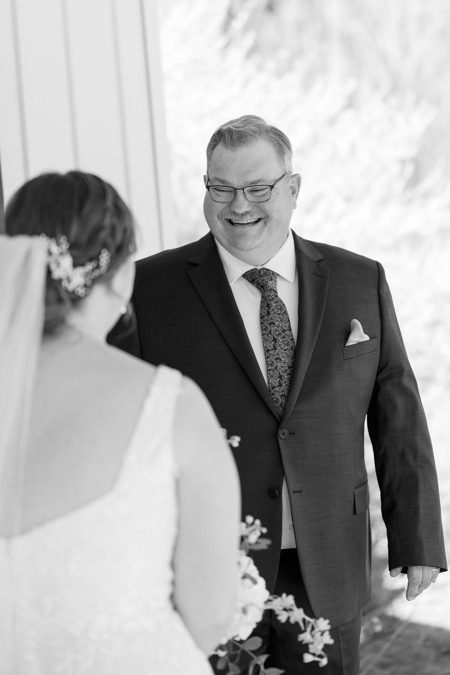 Two people in formal attire smile and laugh together during an emotional wedding day moment.