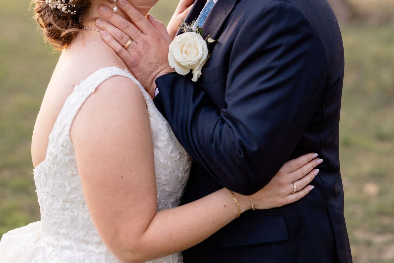 Close-up of couple embracing, with white rose boutonniere on navy suit.