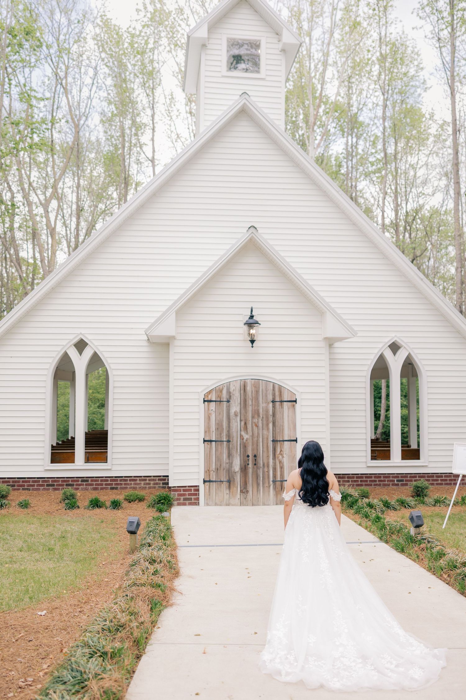Picturesque white chapel with Gothic windows and wooden doors nestled among spring trees.