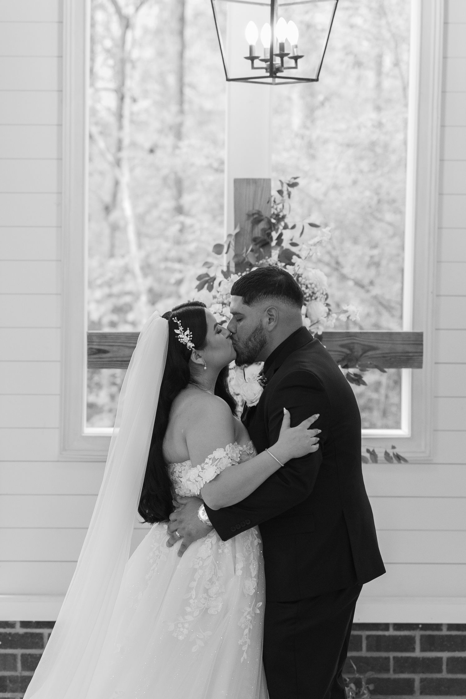Wedding ceremony moment captured in black and white at an elegant indoor venue with large windows.