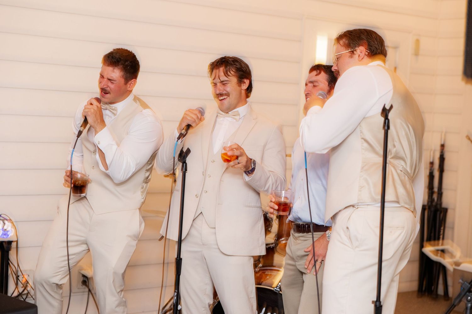 Group wearing light colored suits laughing and celebrating together indoors.