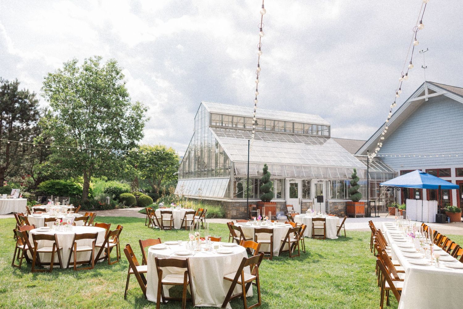 A rustic outdoor wedding venue with white tents, wooden chairs, and lush green landscaping creates an elegant countryside setting.