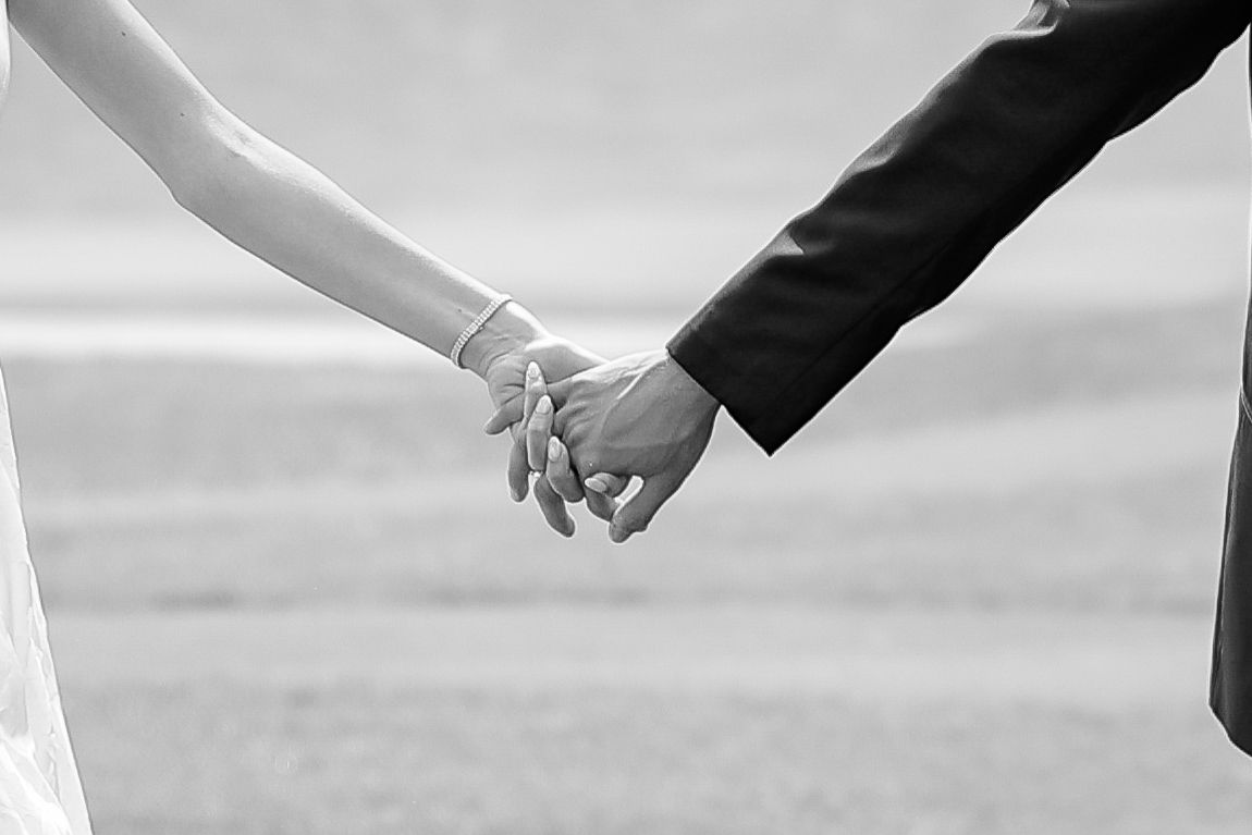 Close-up black and white photo of bride and groom holding hands on their wedding day.