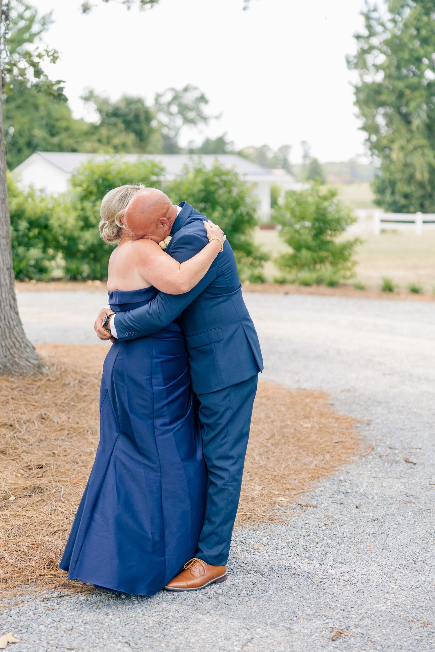 Couple in matching navy outfits sharing a warm embrace outdoors at a wedding.
