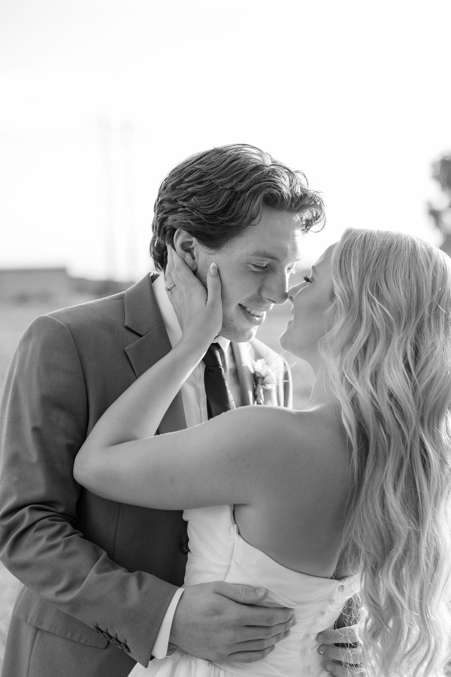 Black and white photo of bride and groom sharing a romantic almost-kiss, bride tenderly holding grooms face.