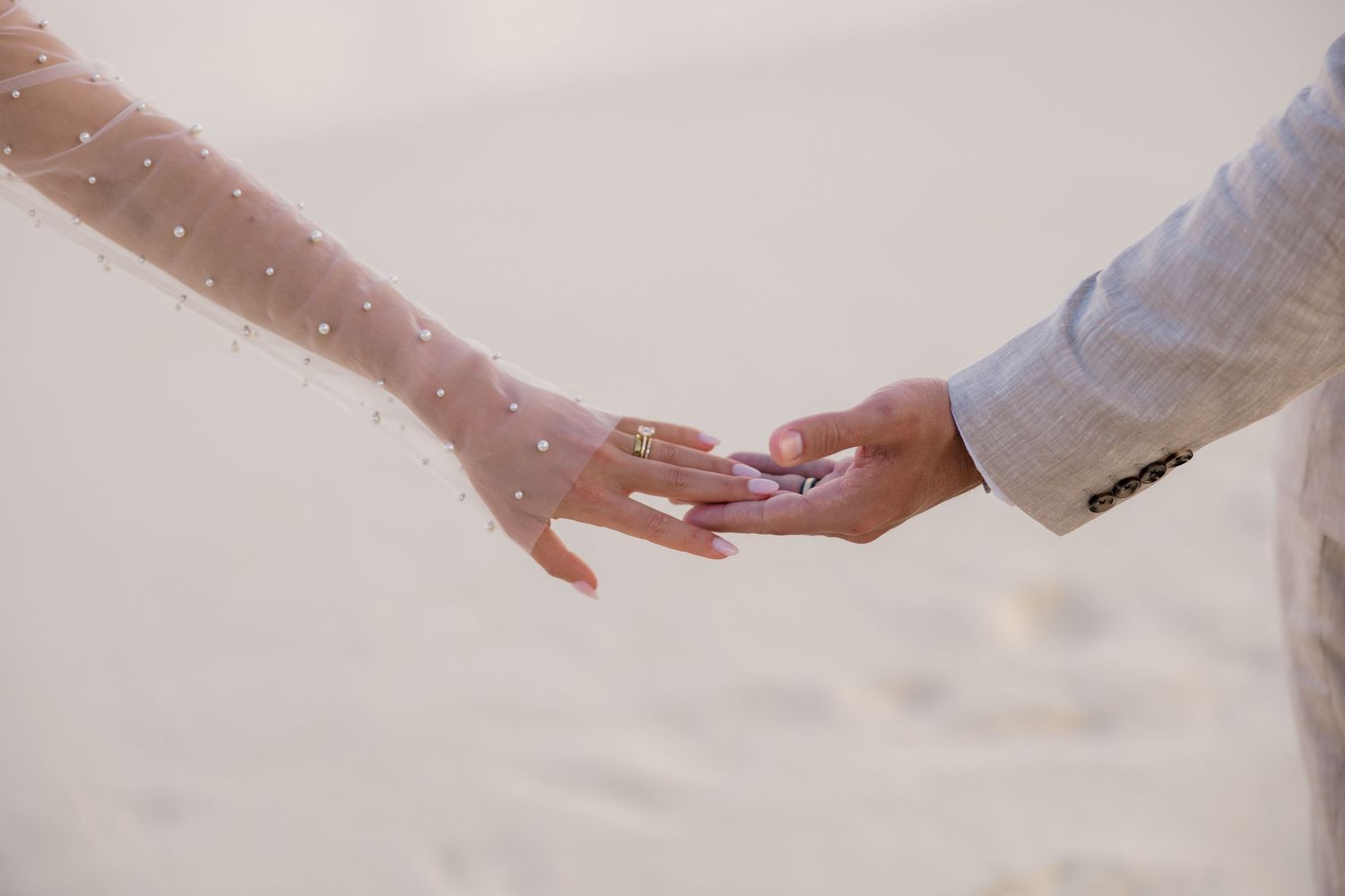 Two hands reaching toward each other against a light background with sparkles in a romantic gesture.