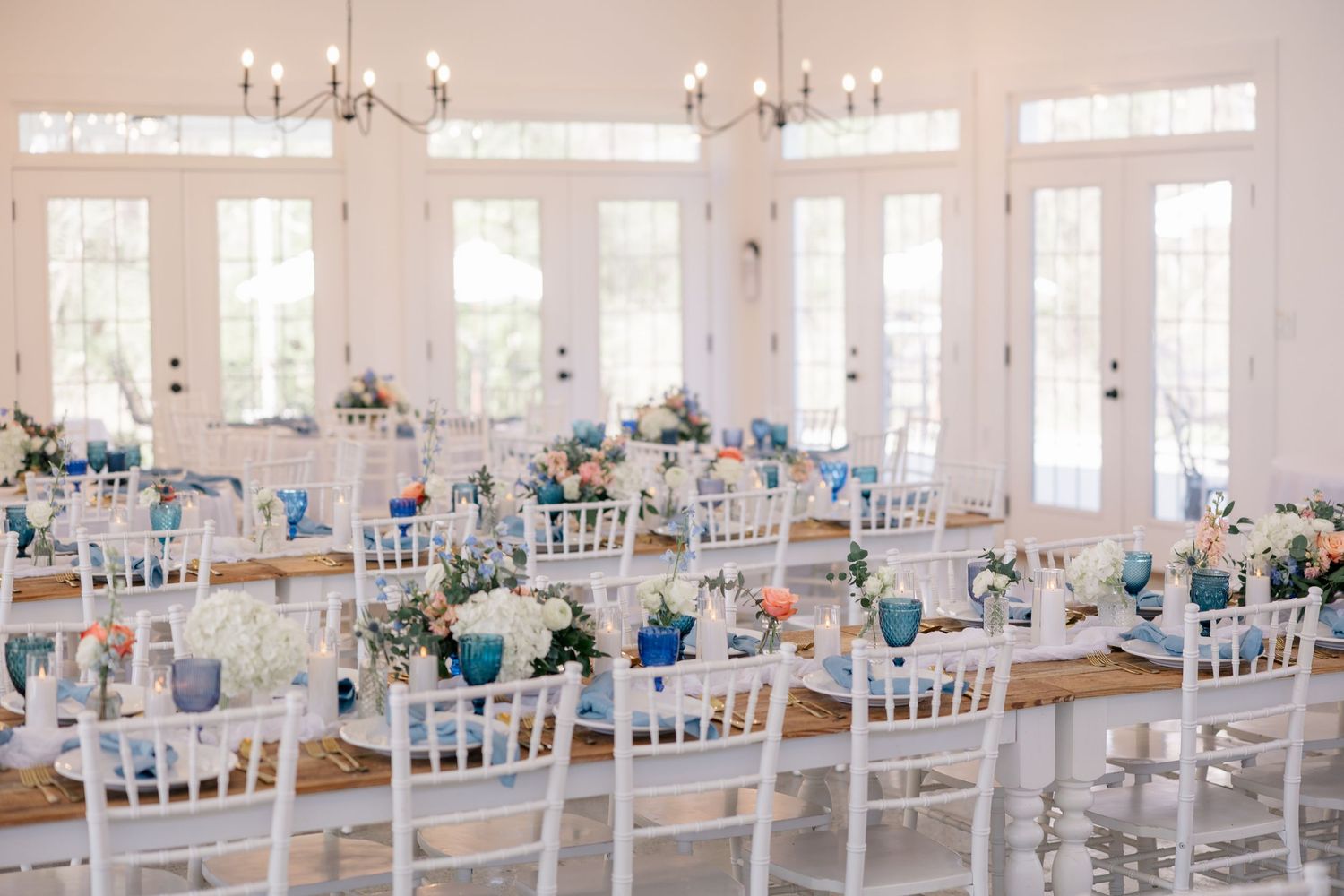 Wedding reception hall decorated in white and blue with elegant table settings and chandeliers.