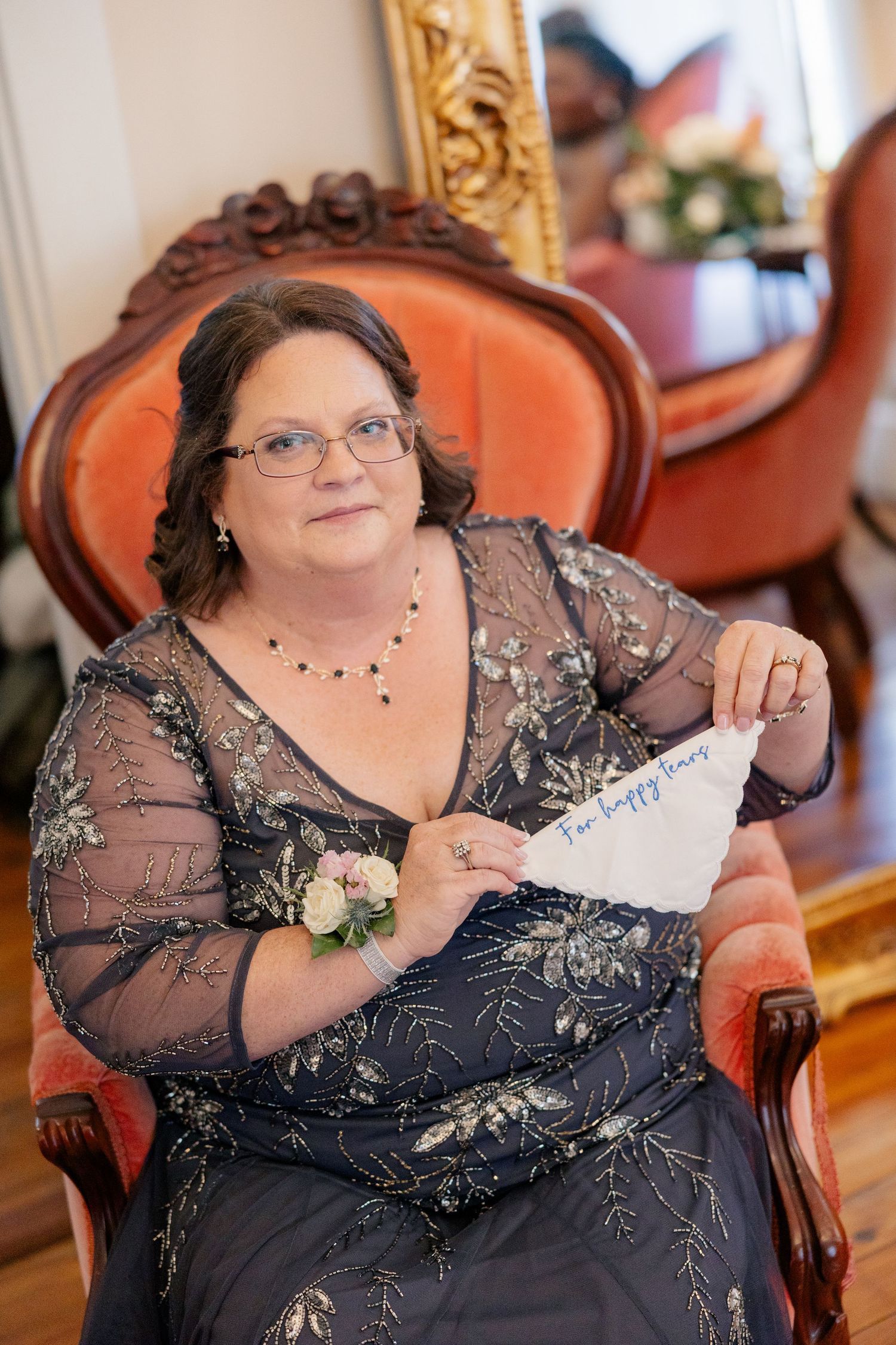 Woman in an embellished navy dress sitting in an ornate chair with a delicate corsage.