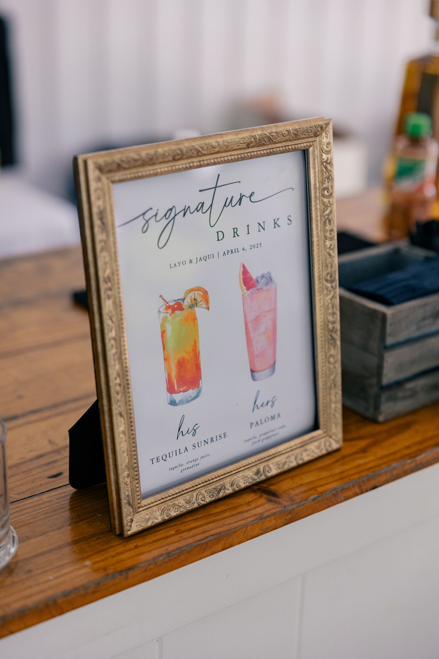 Framed cocktail menu signs displaying colorful drink illustrations on a rustic wooden surface.