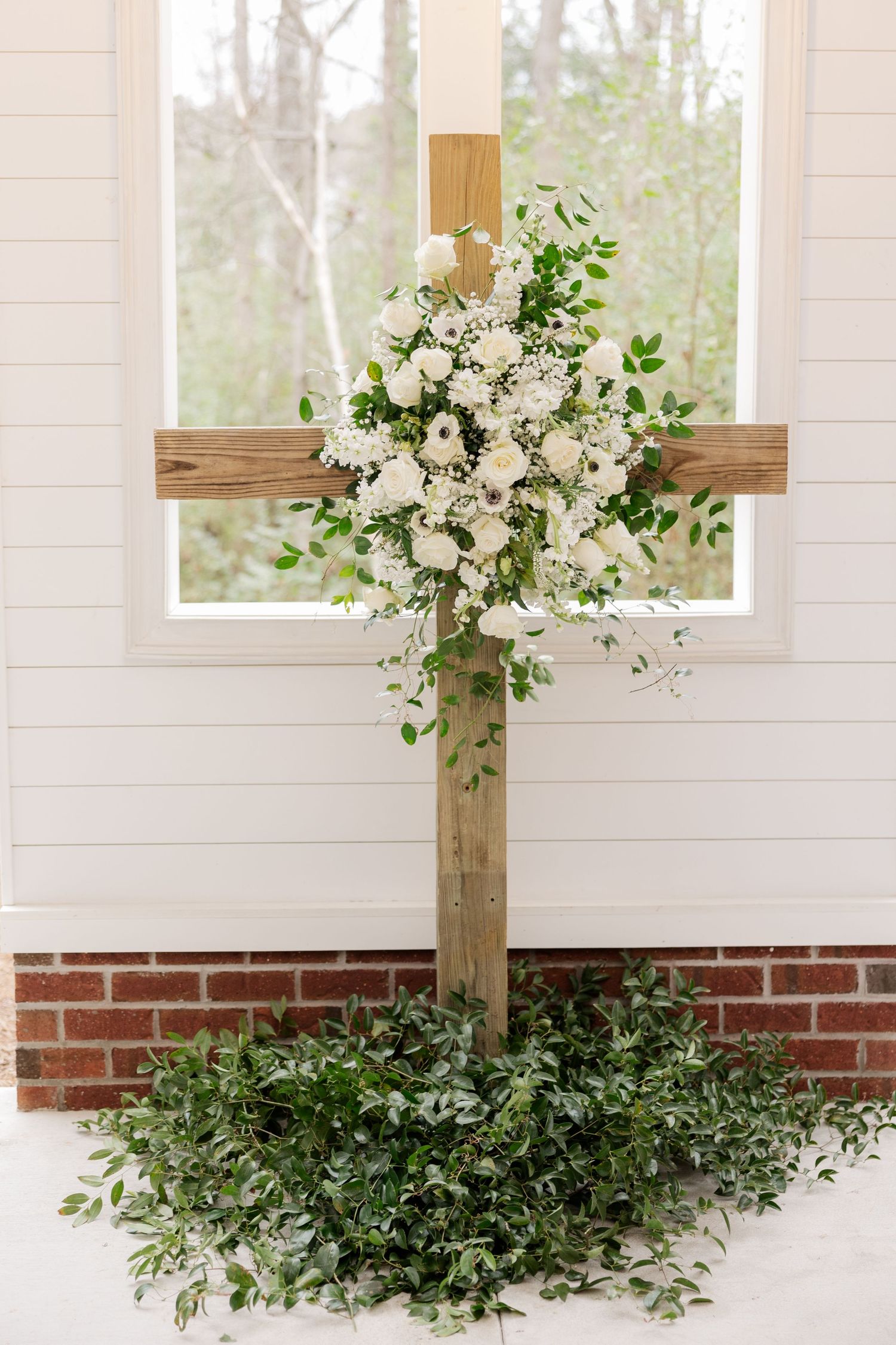 White floral arrangements with greenery decorate wooden crosses against a white paneled wall.