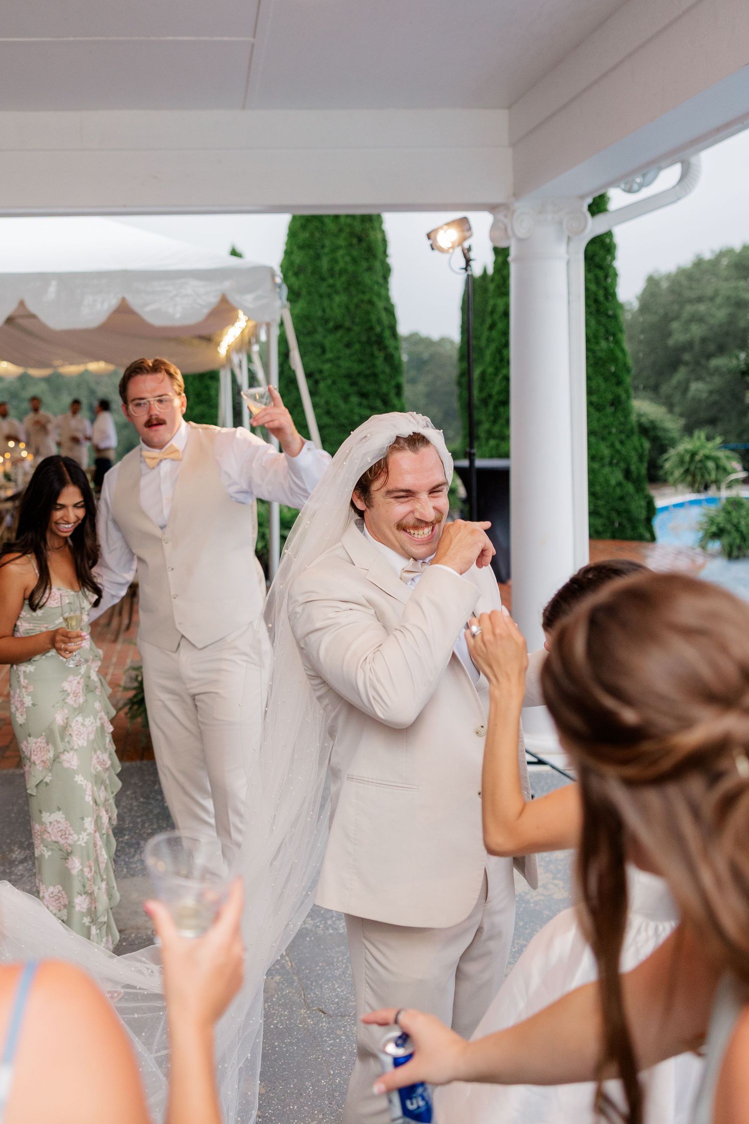 Wedding guests dancing and celebrating together at an outdoor reception under a white covered porch area.