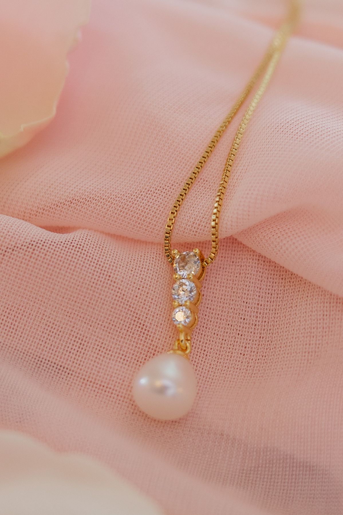 Delicate pearl and crystal pendant necklace on blush pink tulle fabric displayed in closeup detail shots.