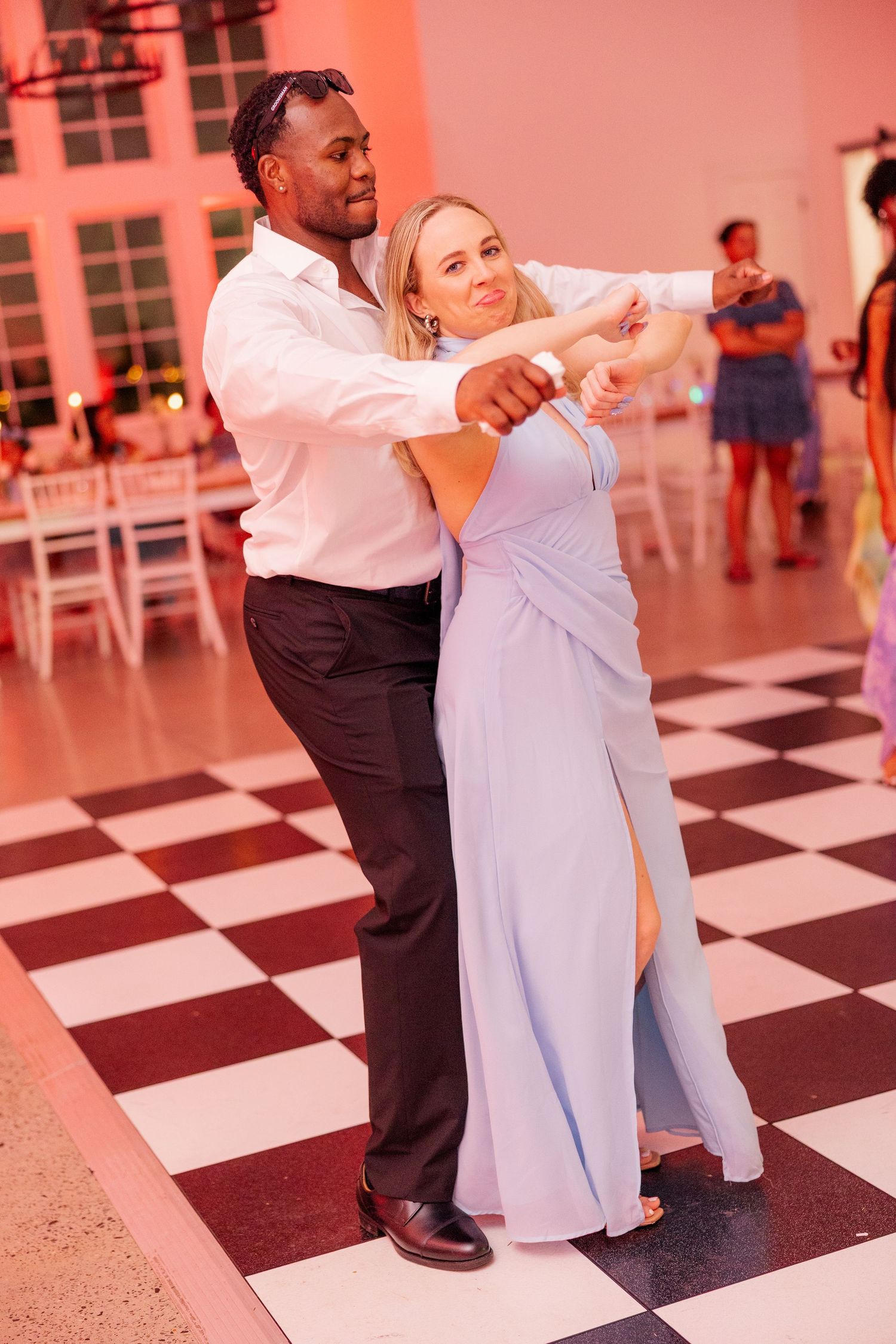 Couple dancing together on a checkered floor with pink ambient lighting.