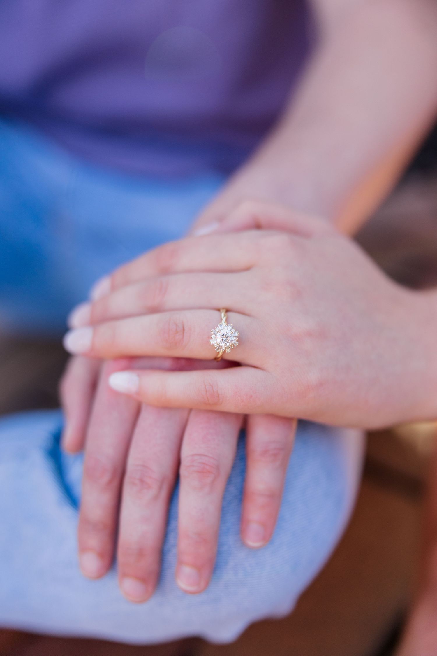 Close-up of hands displaying a sparkling engagement ring against denim.