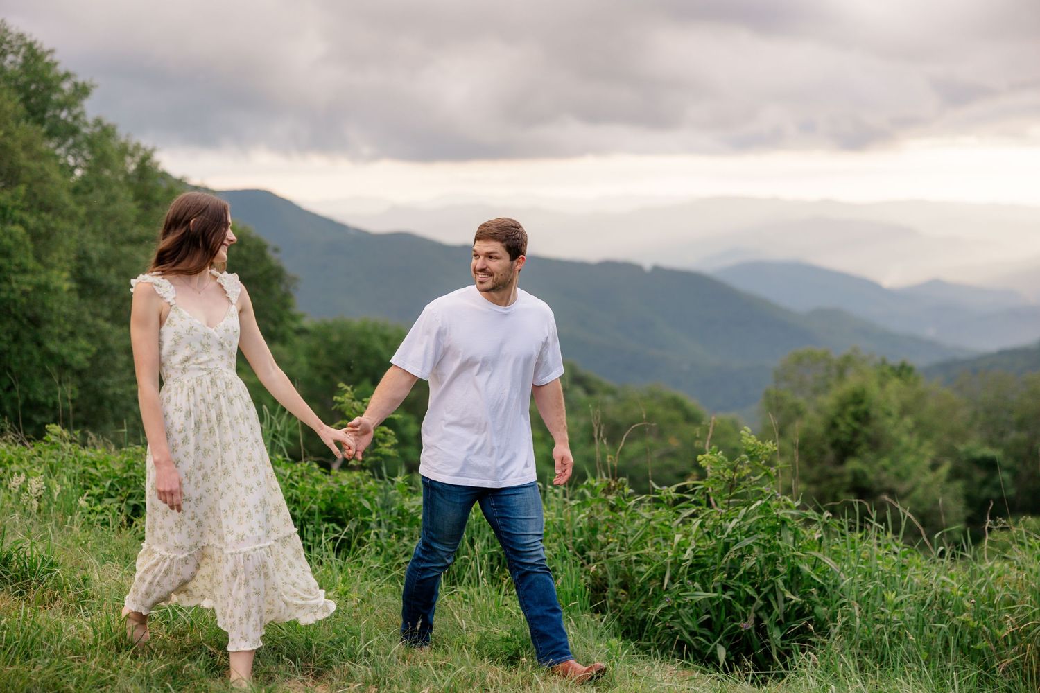 A couple stands together in a lush mountain meadow with misty peaks in the background during a romantic photo session.