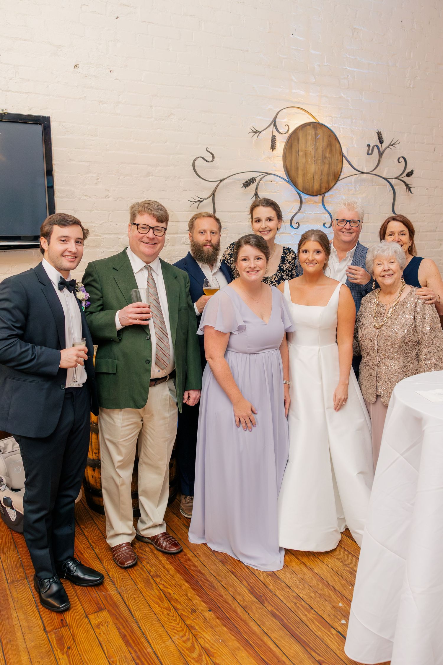 Wedding party poses together smiling in a rustic venue with white brick walls and warm wood floors.