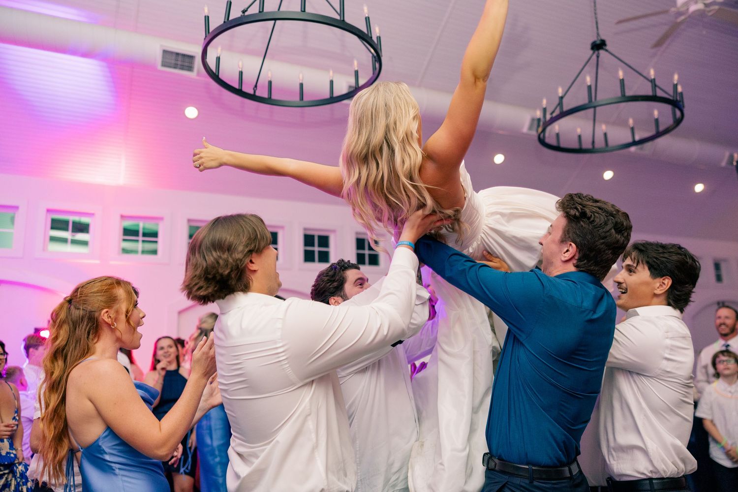 Wedding guests lift the bride in a white dress above the crowd on the dance floor at the reception.