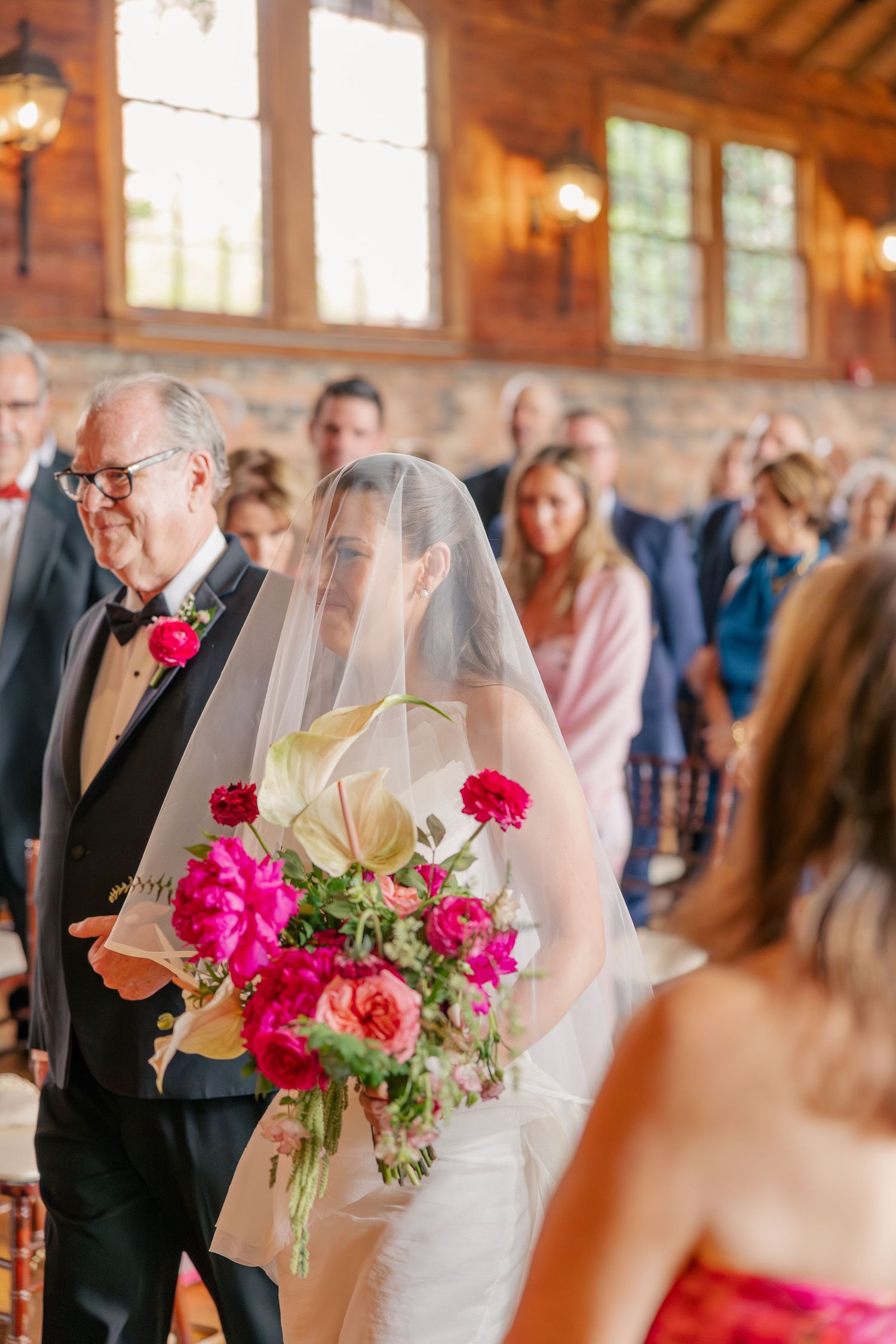 Bride walks down aisle with father holding vibrant pink and white bouquet at wedding ceremony.