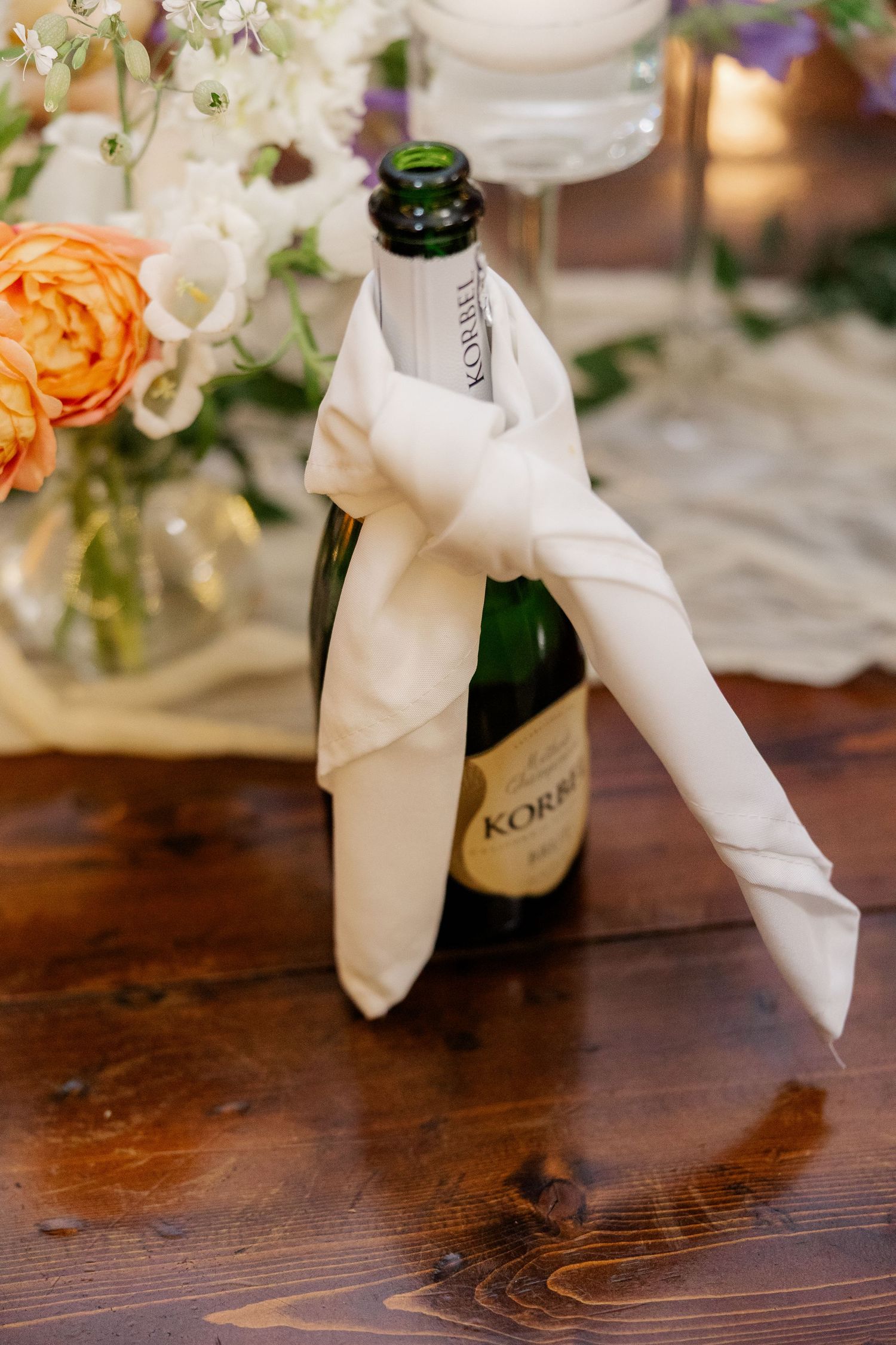 White ribbon-tied wine bottles with floral decorations displayed on wooden surface.