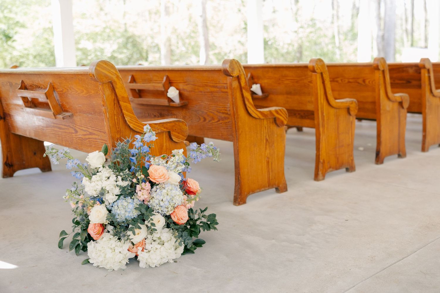 Chapel interior with wooden pews and floral arrangements along the aisle.