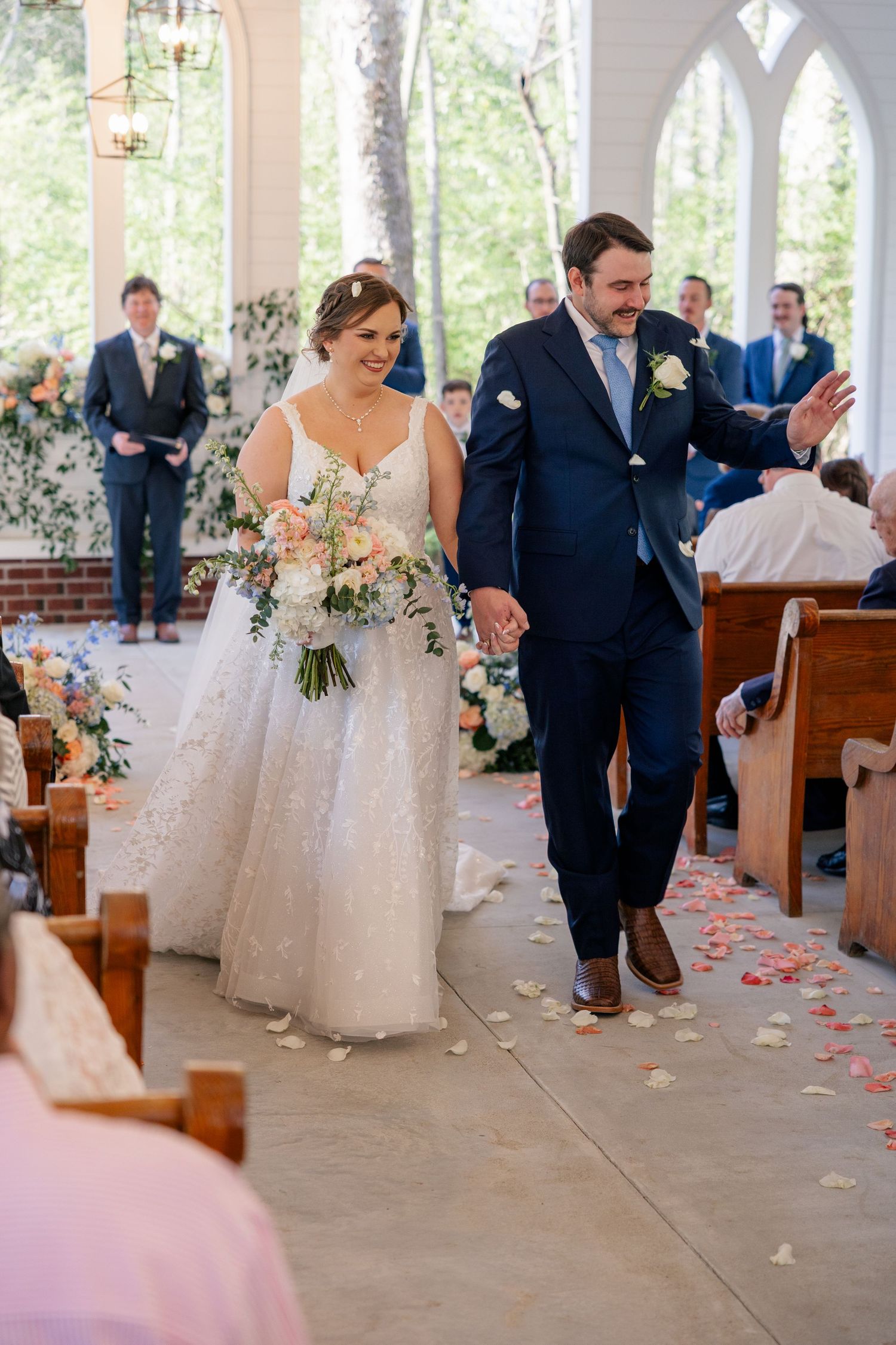 Wedding ceremony recessional in a white chapel with scattered rose petals along the aisle.
