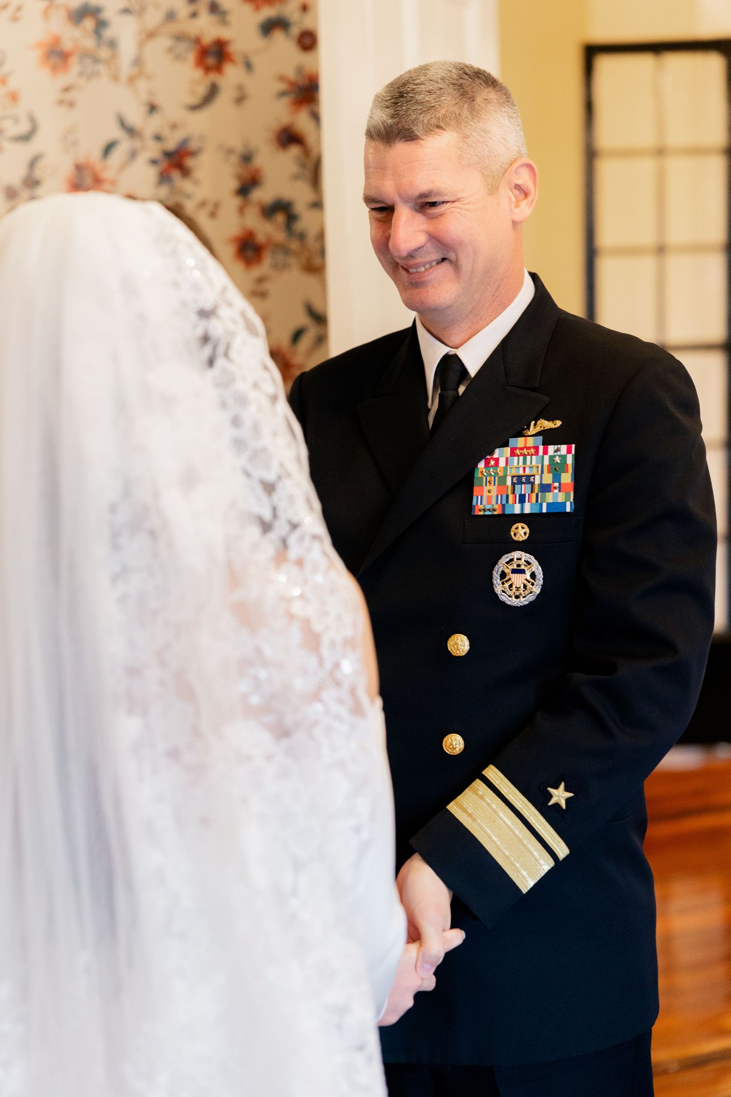 A military officer in dress blues shares a tender moment with a bride in white during their wedding ceremony.