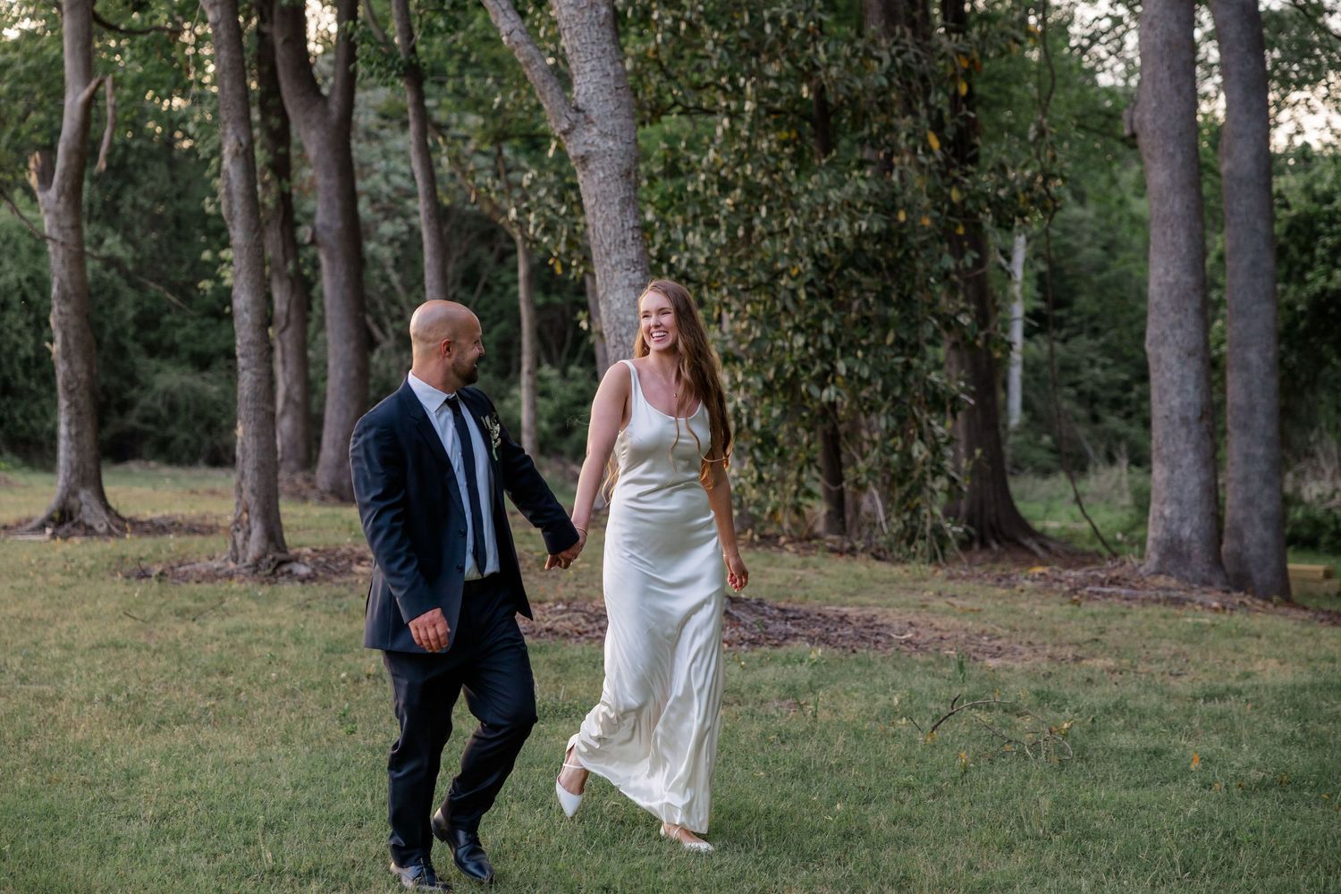 Wedding couple walks hand in hand through a serene wooded area.